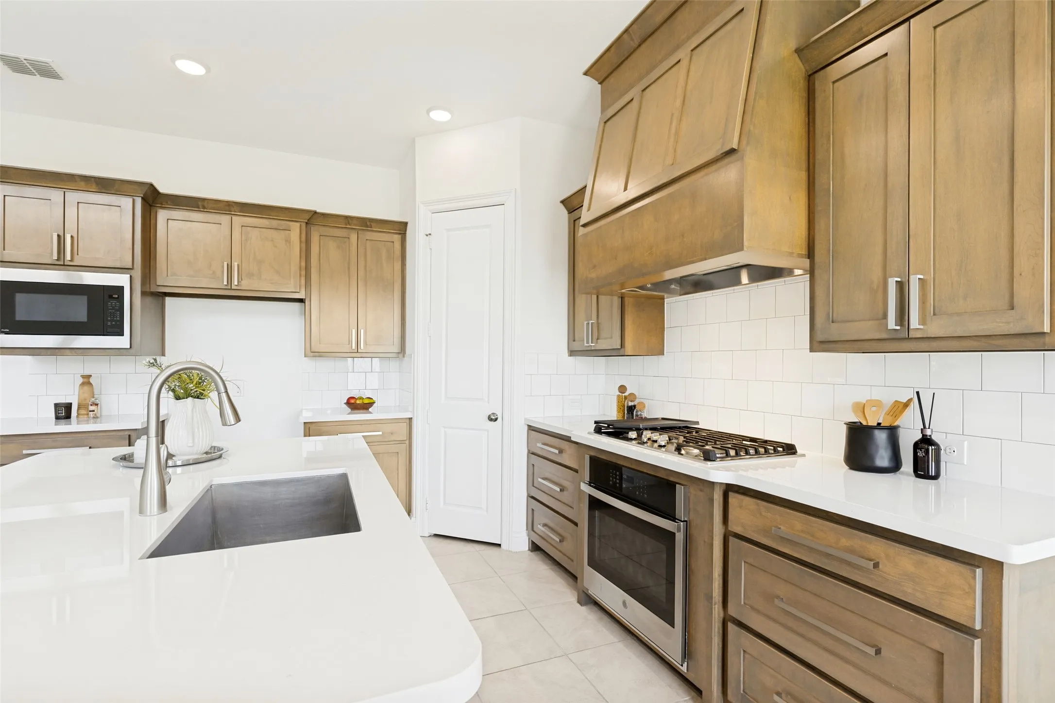 Modern kitchen featuring an undermount stainless steel sink, white countertops, built-in stainless steel appliances, a gas cooktop, and a wood-finish range hood