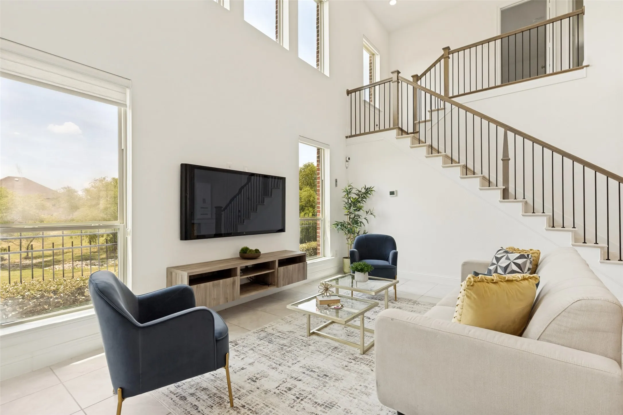 Two-story living area filled with natural lighting from two large windows, showcasing this staircase with dark metal balusters and wood-finish handrails