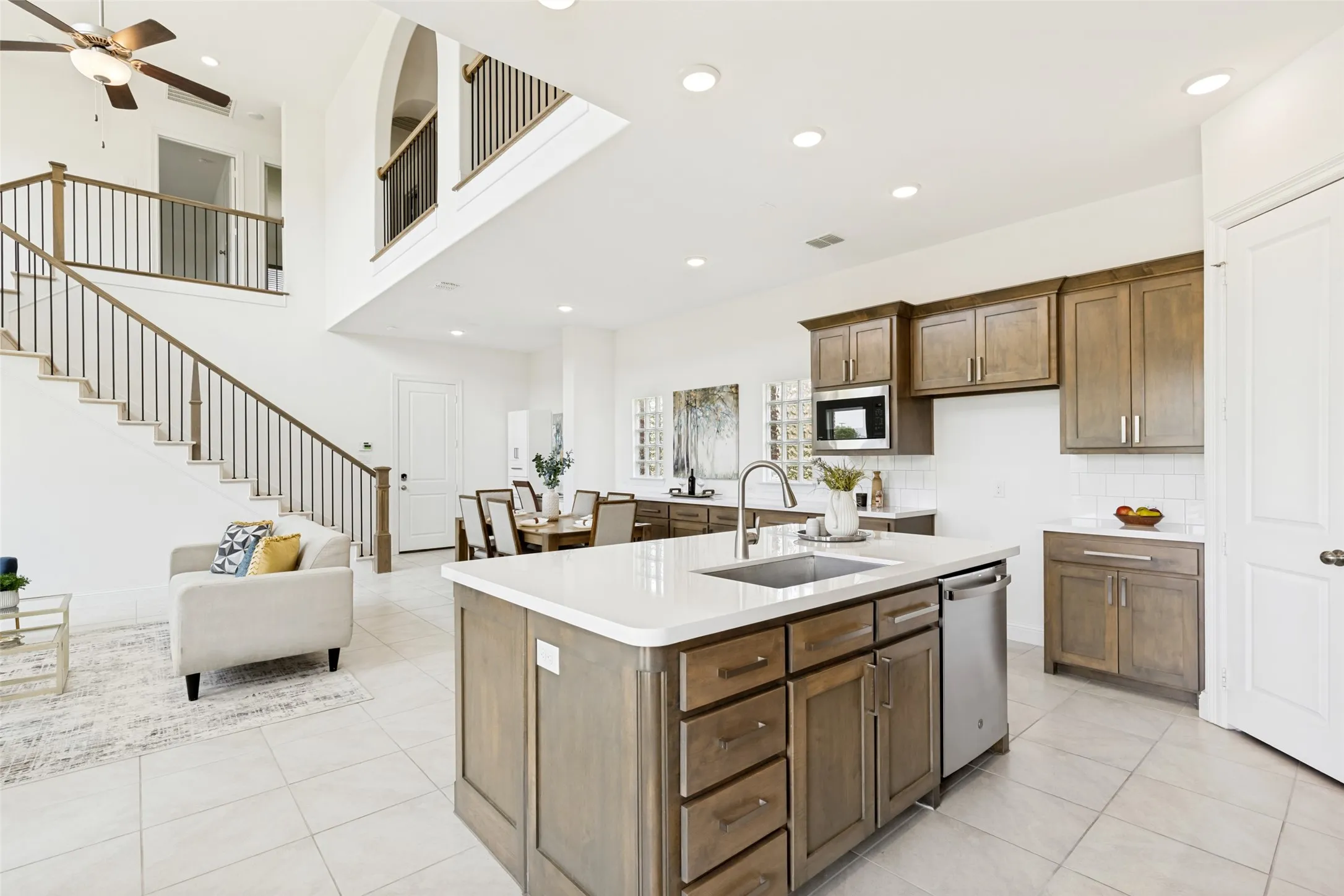 Expansive open-concept living space featuring a central kitchen island with an undermount sink, wood-finish cabinetry, stainless steel appliances, and recessed lighting