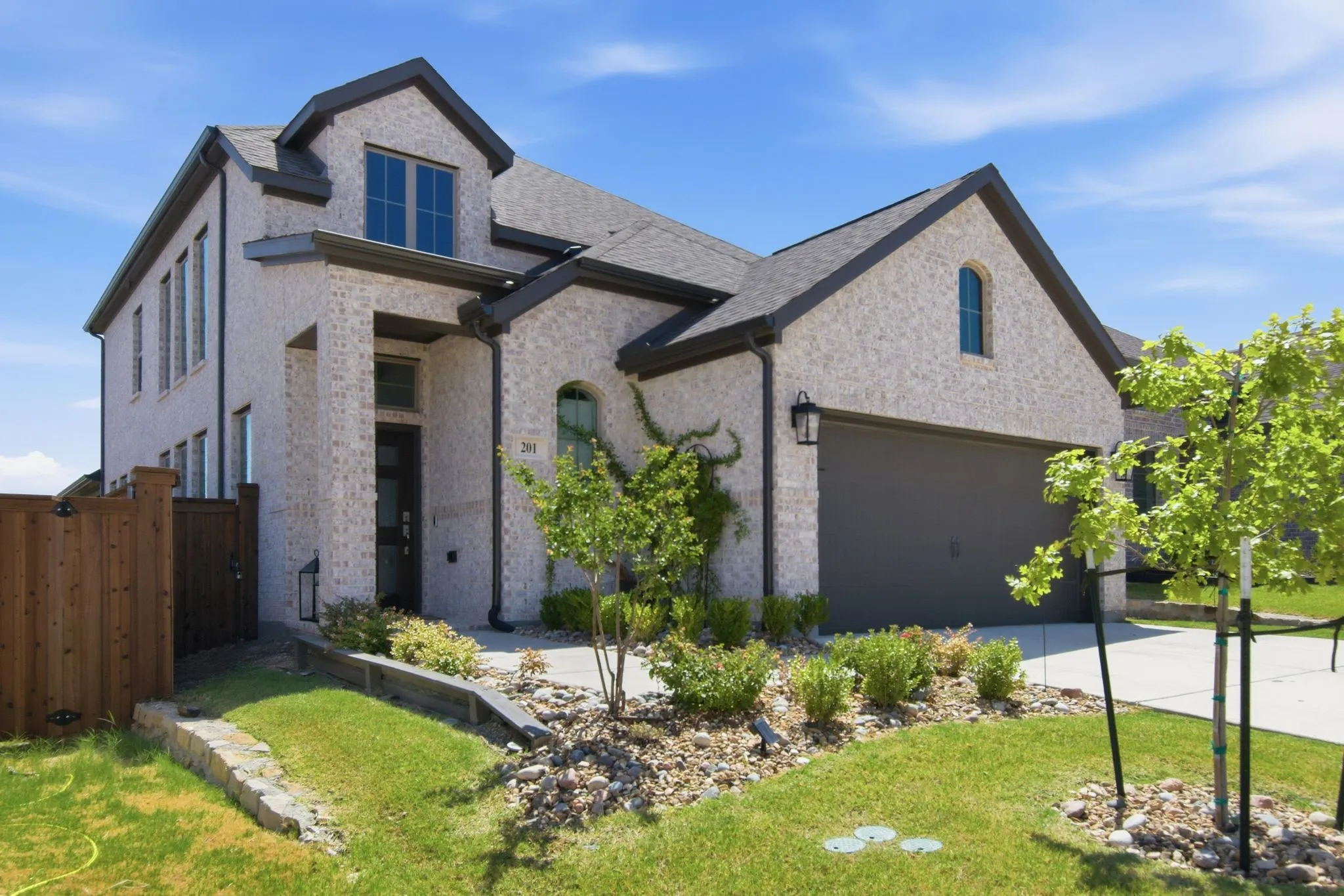 Contemporary two-story residence featuring a light-colored brick exterior, a dark shingle roof, and a two-car garage