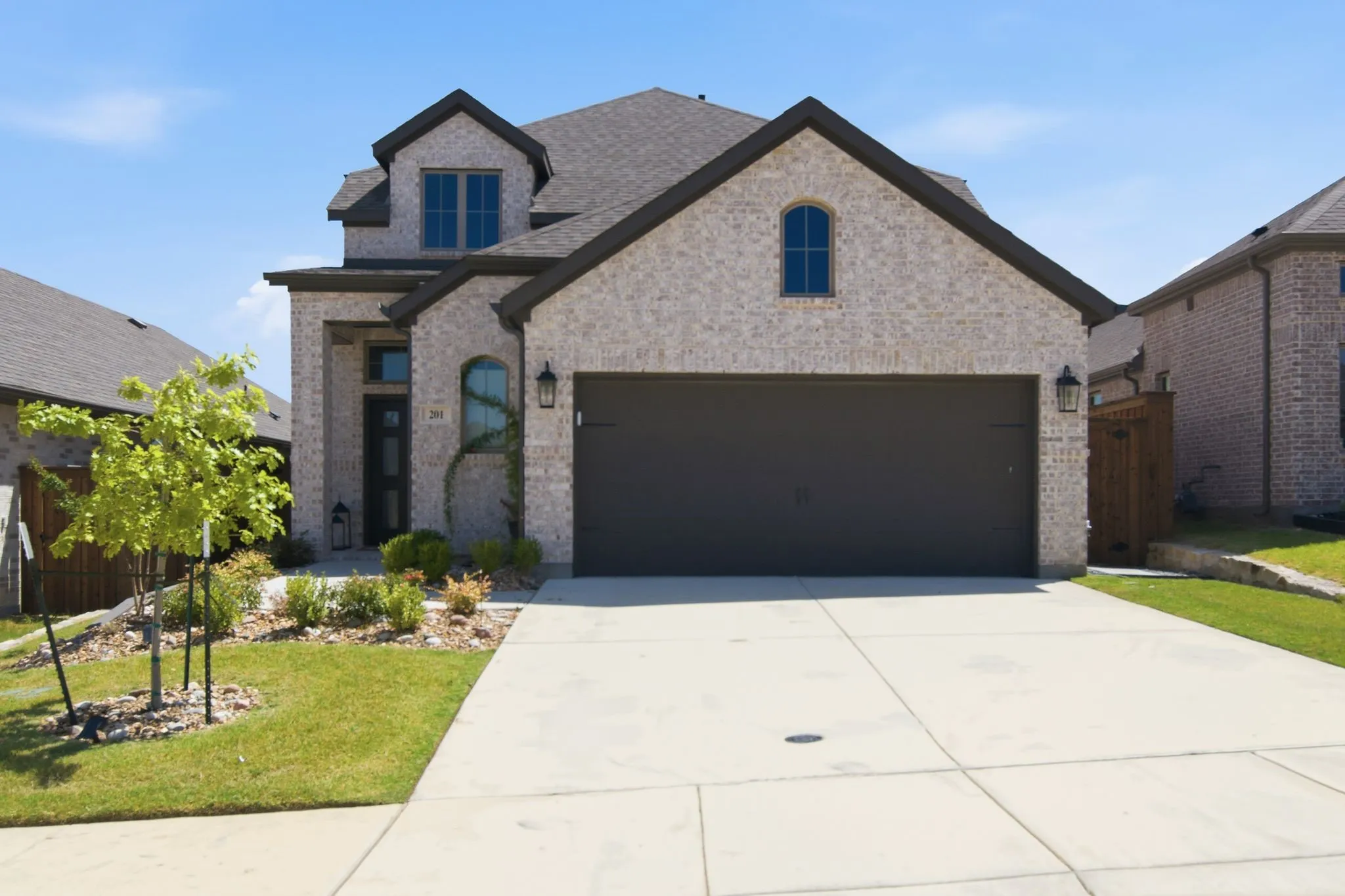 Two-story brick exterior featuring a dark asphalt shingle roof, attached two-car garage, arched entryways, and a concrete driveway