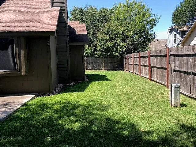 Expansive backyard featuring a manicured lawn, a full wood privacy fence, and a concrete patio slab