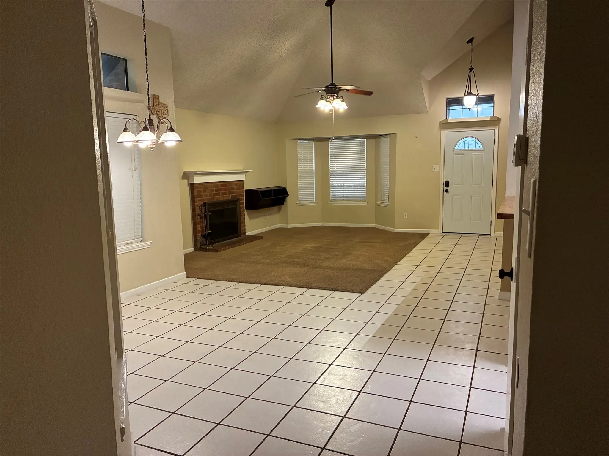 Vaulted ceilings, brick fireplace, bay window, ceiling fan, and white tile flooring