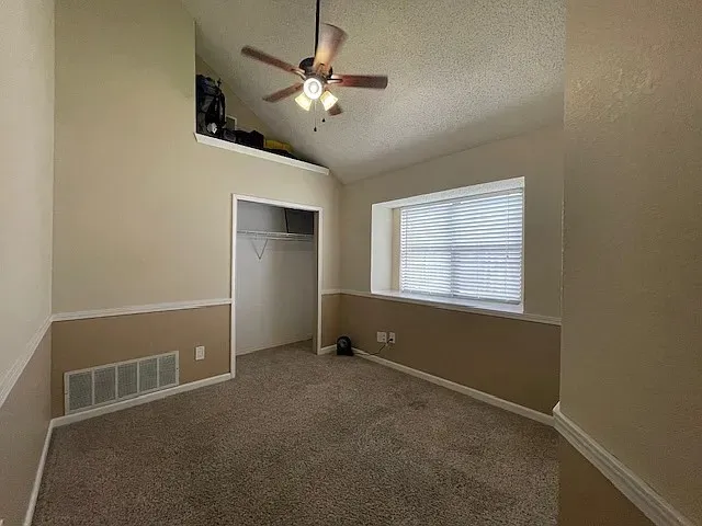 Carpeted room featuring a vaulted ceiling and an integrated ceiling fan
