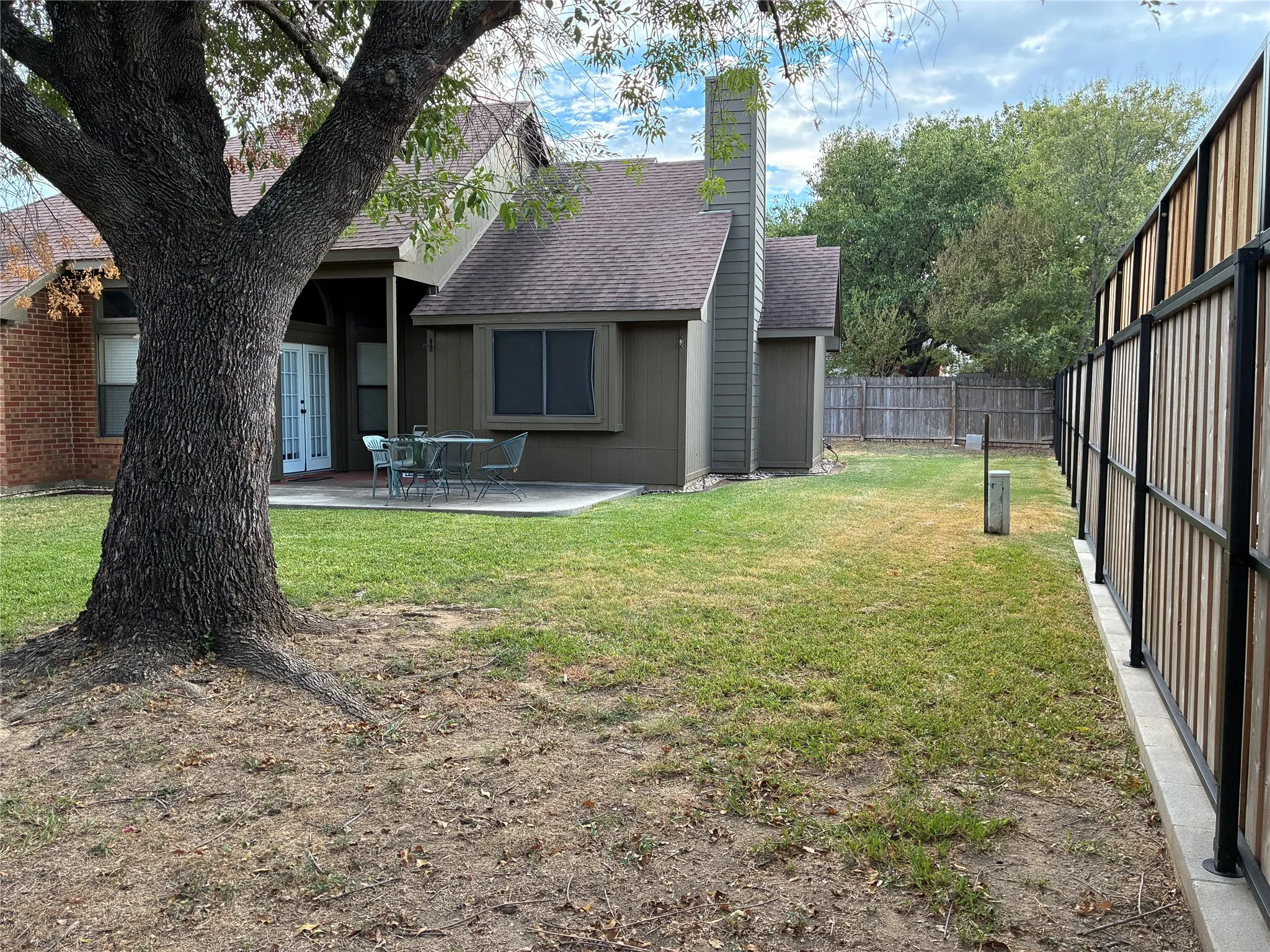 Expansive backyard with a concrete patio, wood-paneled and brick exterior, and a privacy fence