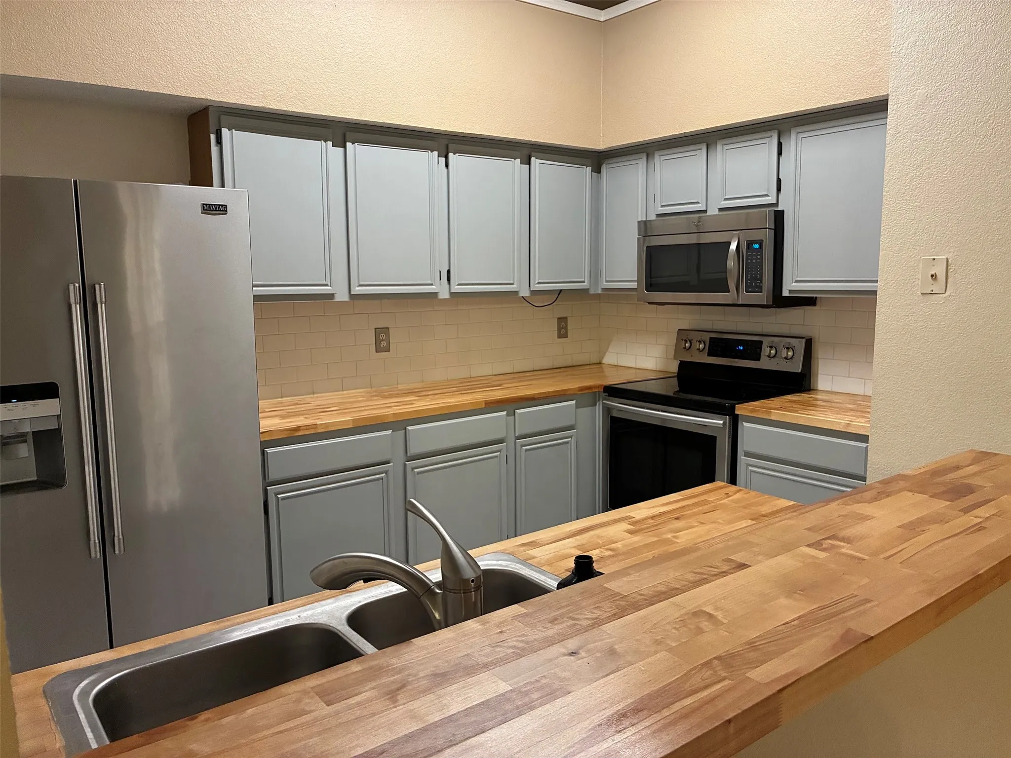 Kitchen featuring light blue cabinetry, wood-finish countertops, stainless steel appliances, and a subway tile backsplash