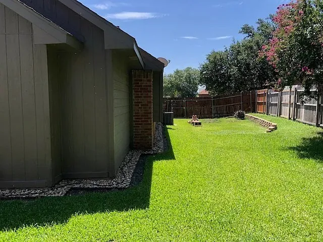 Spacious backyard featuring a lush green lawn, wood privacy fencing, and mature trees