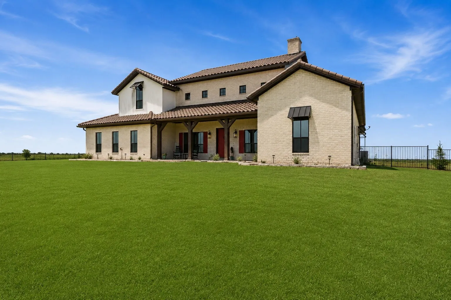Mediterranean-style residence featuring a stucco and light brick exterior, terracotta roof tiles, and an expansive green lawn