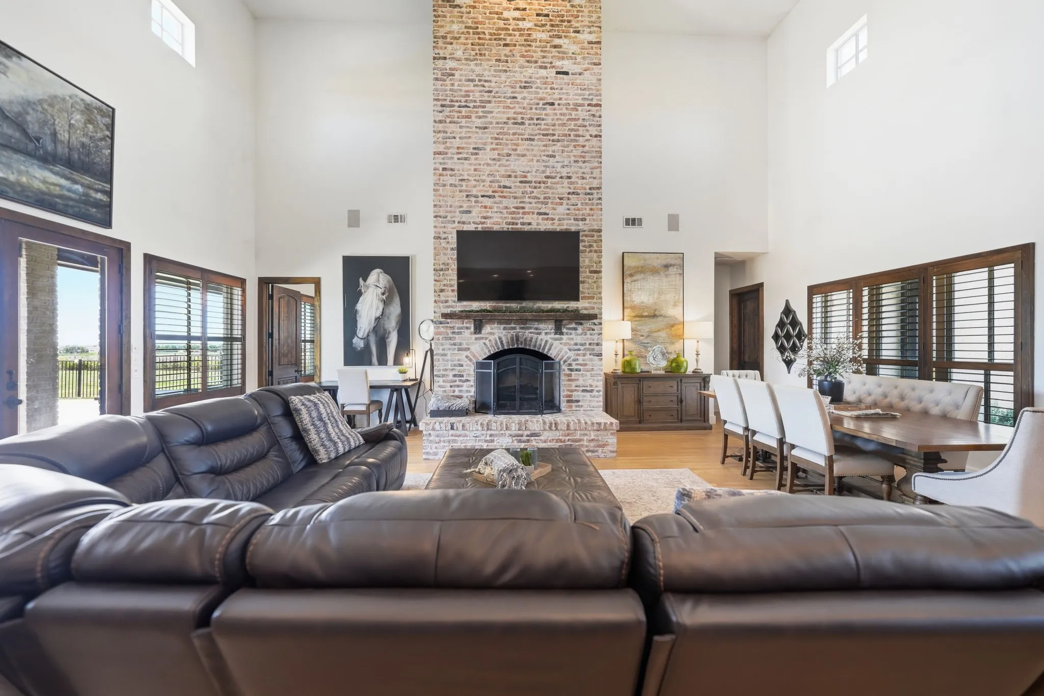 Spacious living area featuring a floor-to-ceiling brick fireplace with an arched firebox, high vaulted ceilings, and wood-finish flooring
