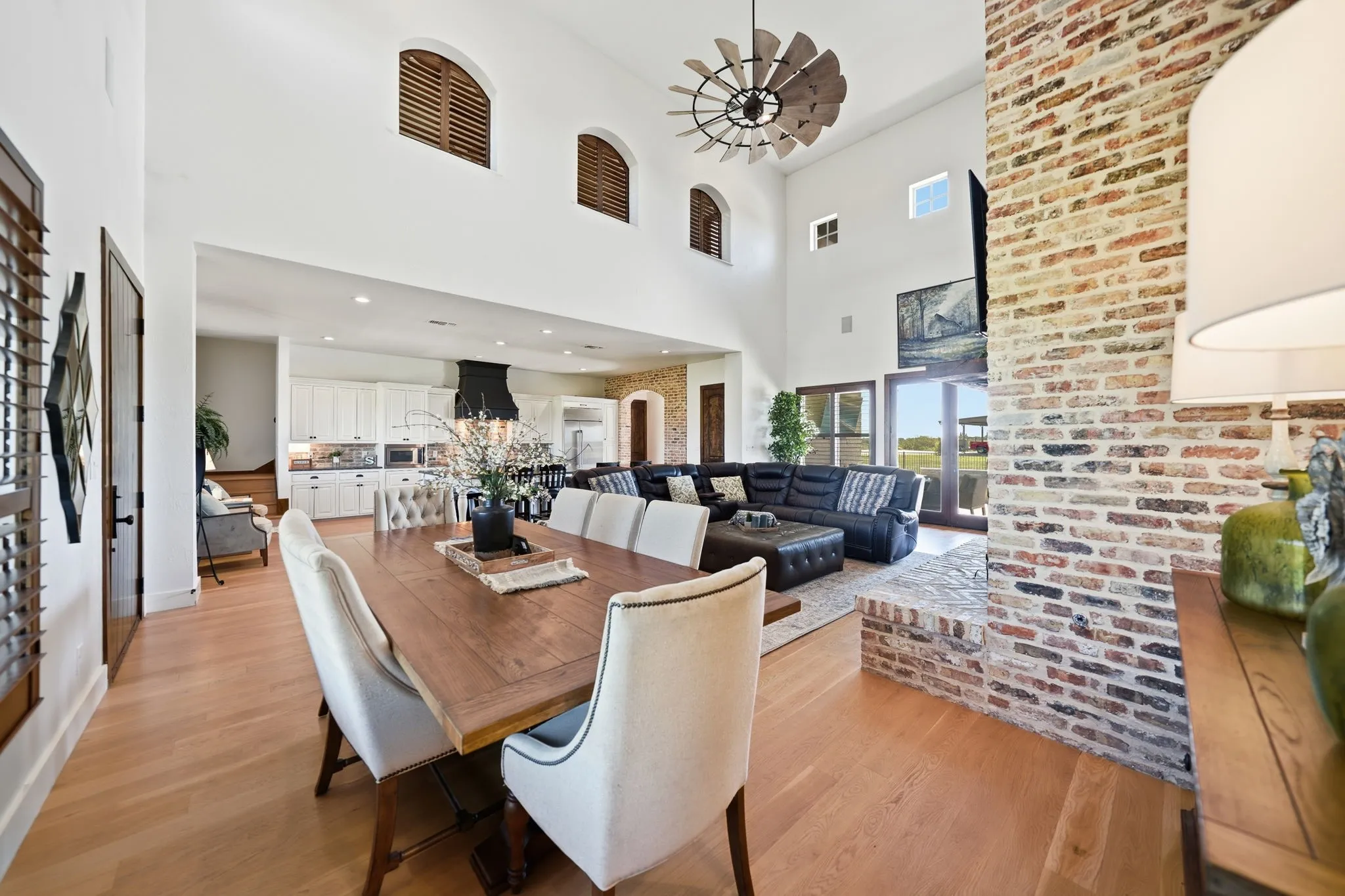 Open-concept living space featuring high vaulted ceilings, light wood-finish flooring, and a prominent brick-clad fireplace