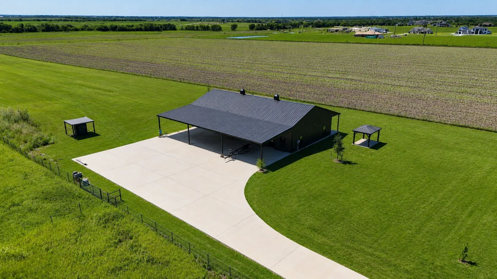 Black metal-sided structure with a dark shingled roof, featuring an extended covered patio and a curved concrete driveway
