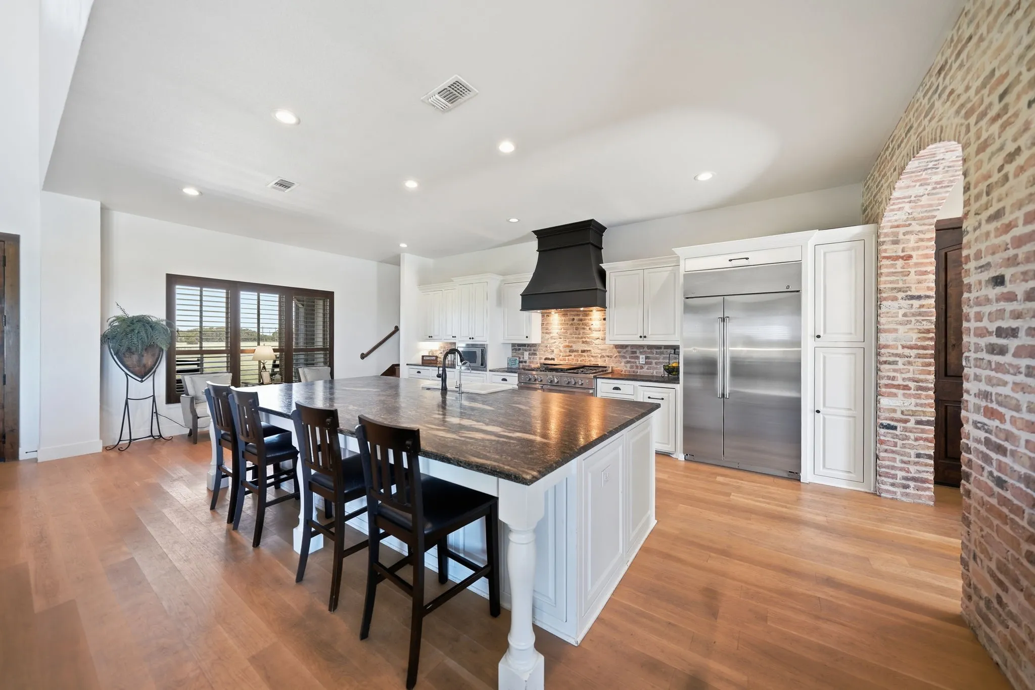 Spacious kitchen featuring a large island with seating, stainless steel appliances, white cabinetry, and wood-finish flooring