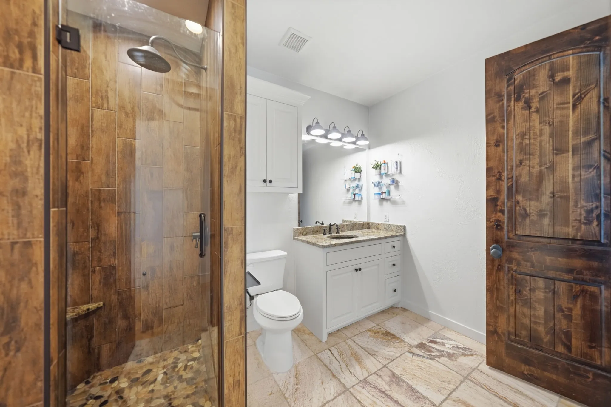 Glass-enclosed shower with wood-look tile walls and a pebble-stone floor