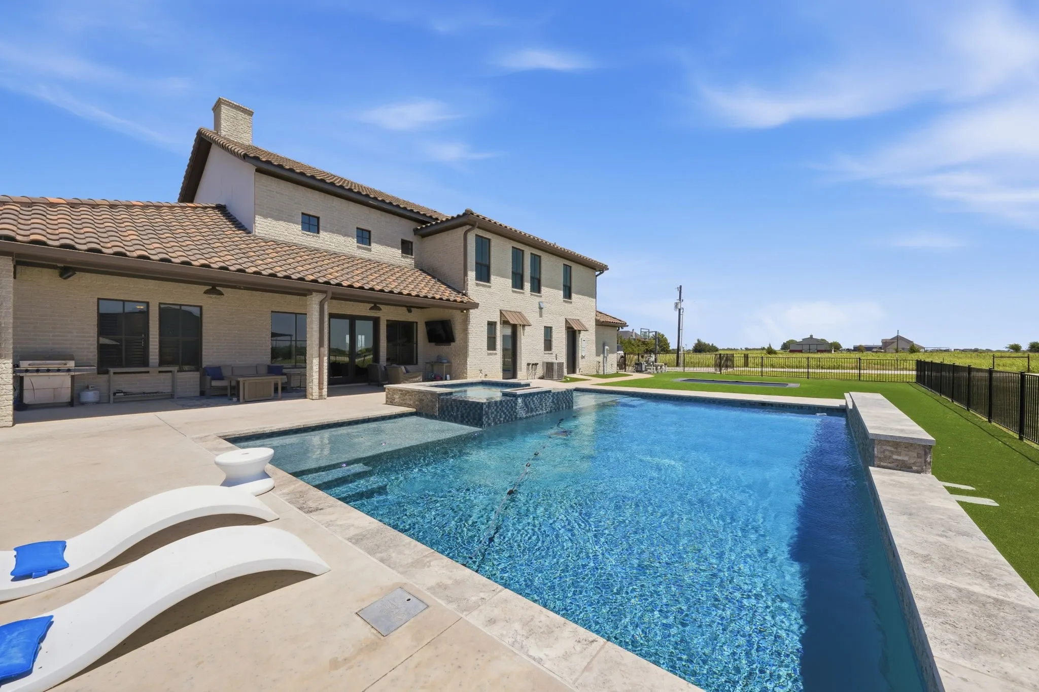 Expansive backyard featuring a blue-tiled swimming pool with integrated spa, broad concrete patio, and an outdoor kitchen with built-in grill