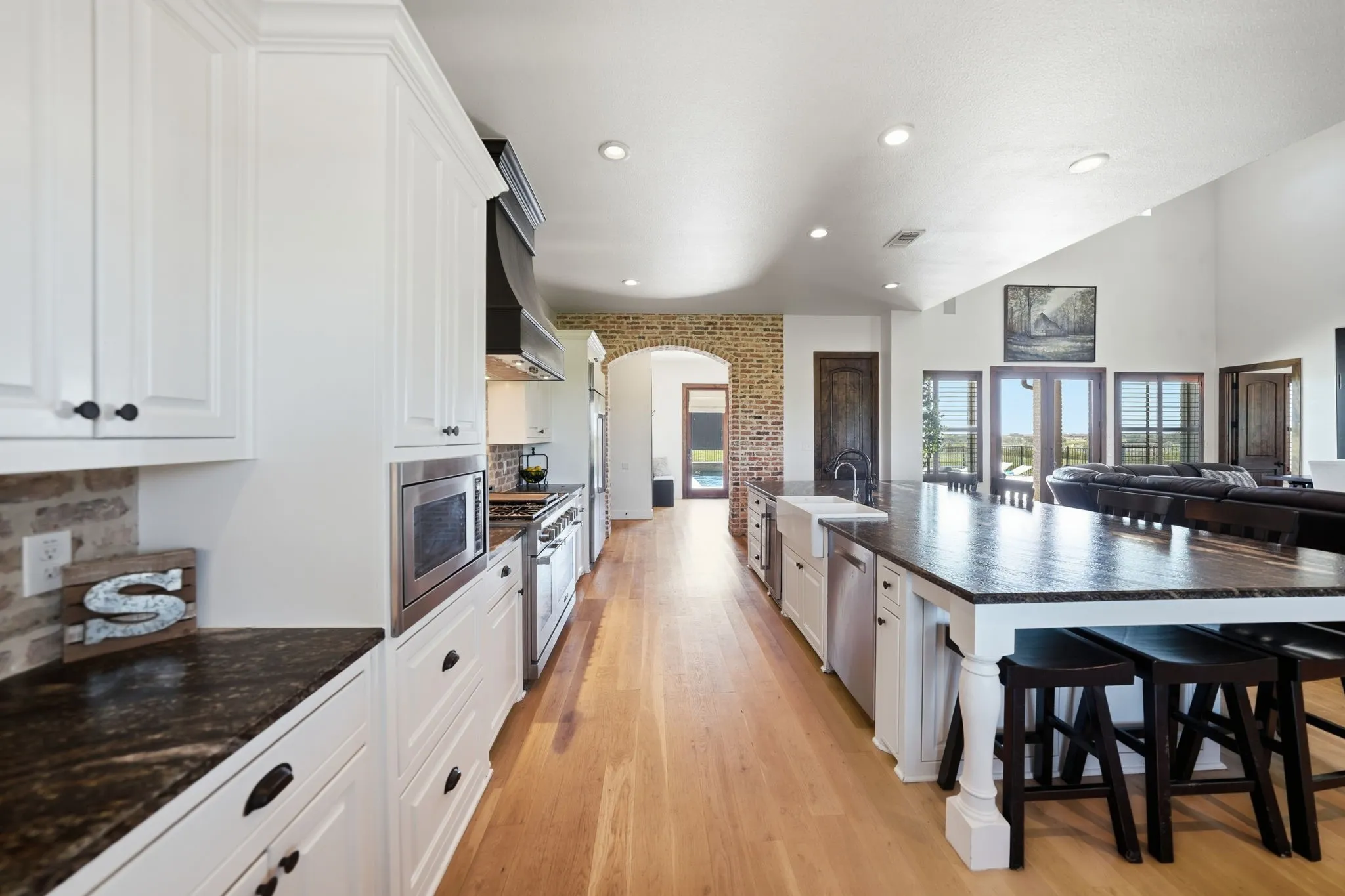 Gourmet kitchen featuring white cabinetry, dark stone countertops, stainless steel appliances, and wood-finish flooring