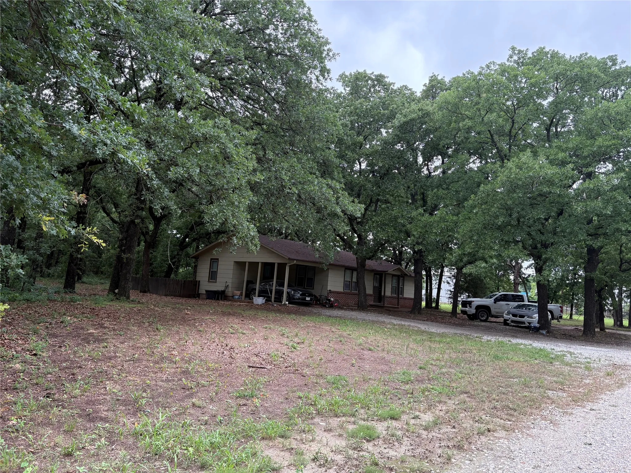 Ranch-style residence featuring a covered porch, a gravel driveway, and mature oak trees