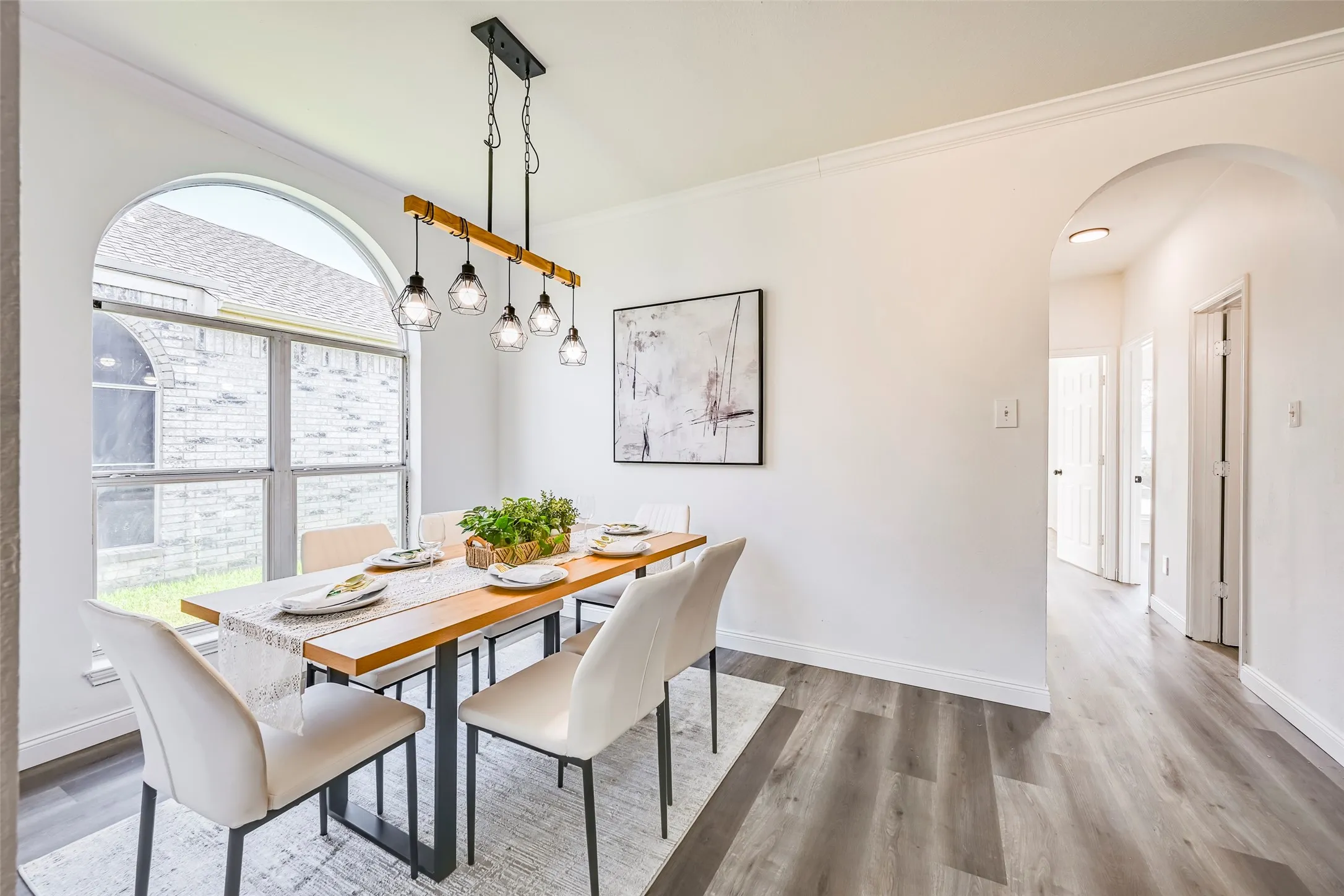 Dining area featuring an arched window, wood-finish flooring, crown molding, and an open archway