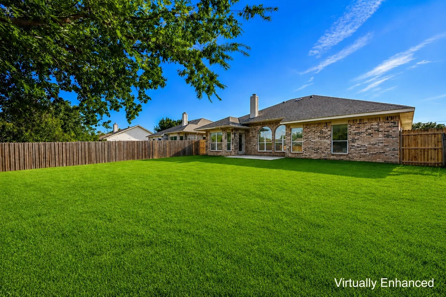 Expansive backyard with a manicured lawn, full privacy fencing, a covered patio, and large windows offering natural illumination to interior spaces