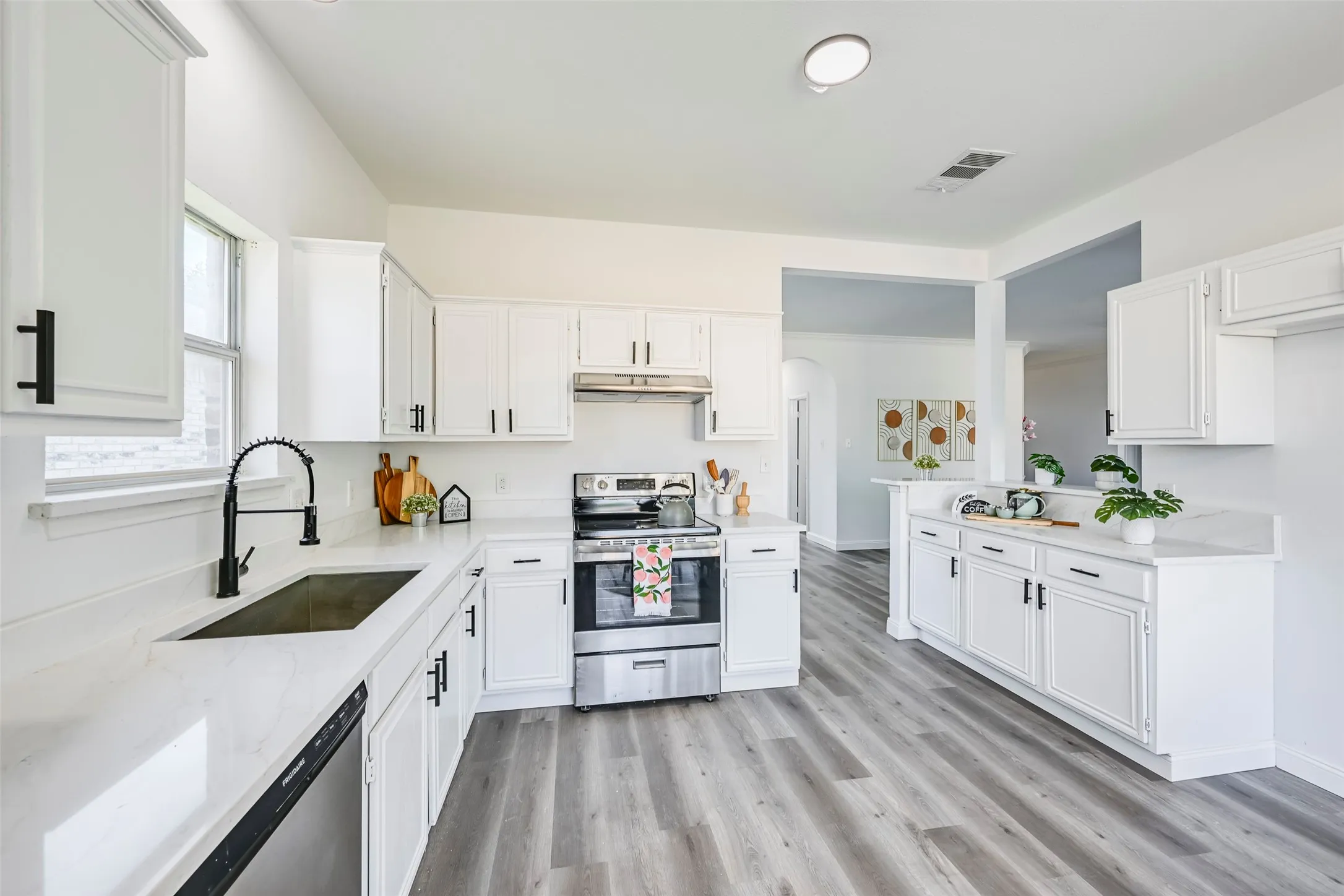 Bright kitchen featuring white cabinetry, light countertops, wood-finish flooring, a stainless steel range, and a black gooseneck faucet