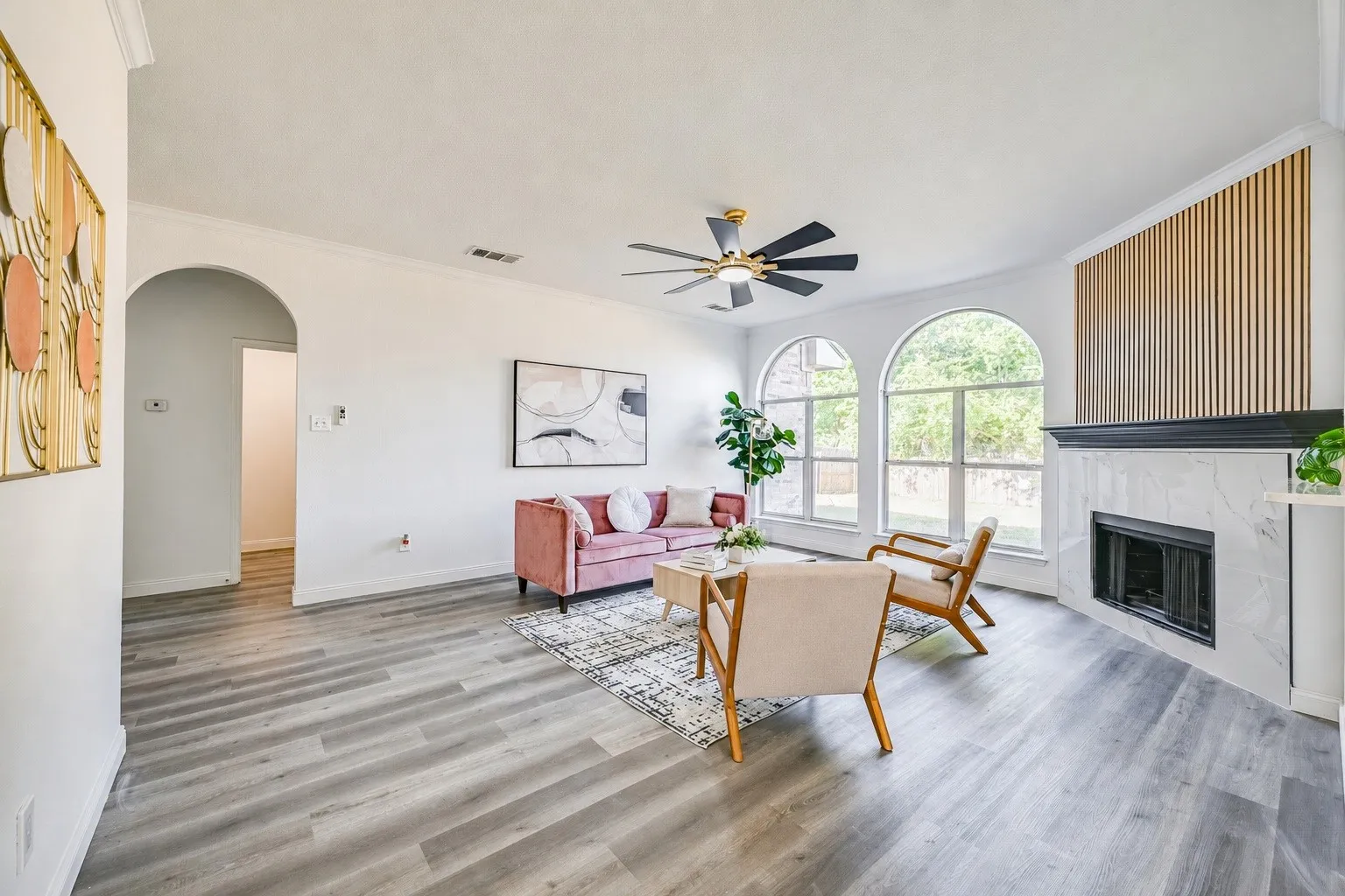 Spacious living area featuring wood-finish flooring, a fireplace with a white marble surround and black mantel, and a decorative slatted wall accent
