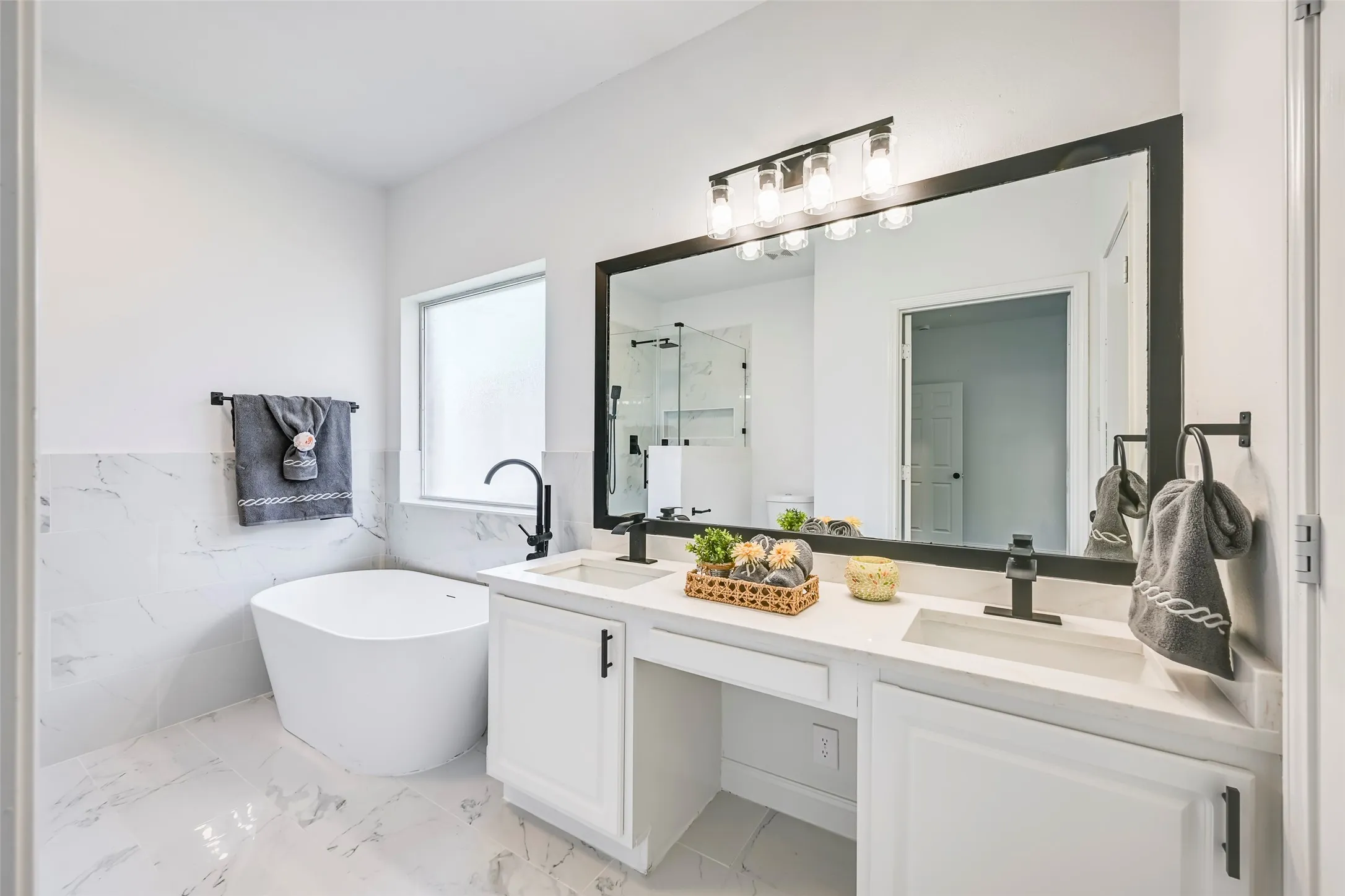 Bathroom featuring a freestanding soaking tub, dual vanity with undermount sinks, and a large framed mirror with overhead lighting