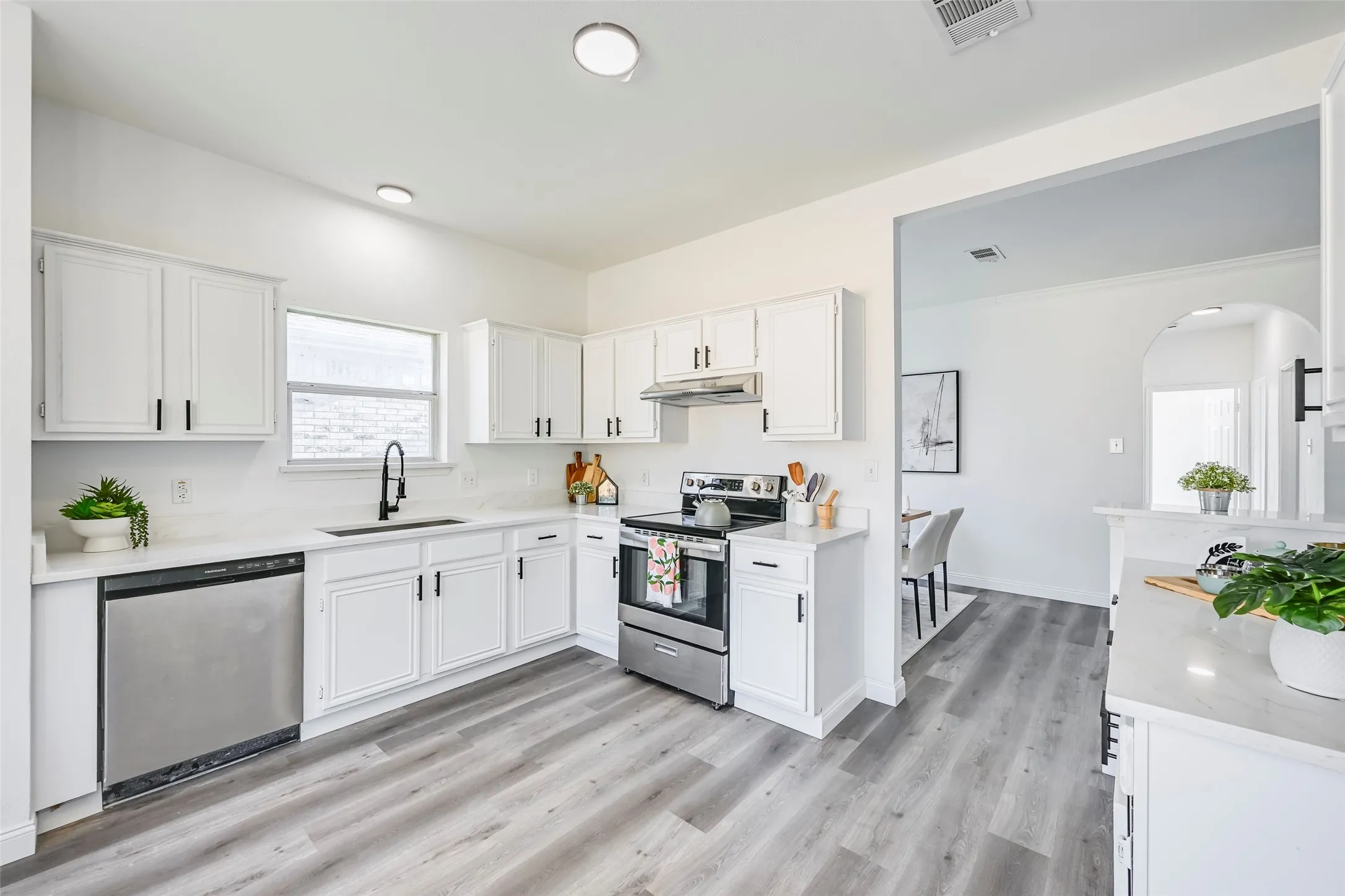 Renovated kitchen featuring white cabinetry, stainless steel appliances, light-toned countertops, a black gooseneck faucet, and wood-finish​​‌​​​​‌​​‌‌​‌‌​​​‌‌​‌​‌​‌​​​‌​​ flooring