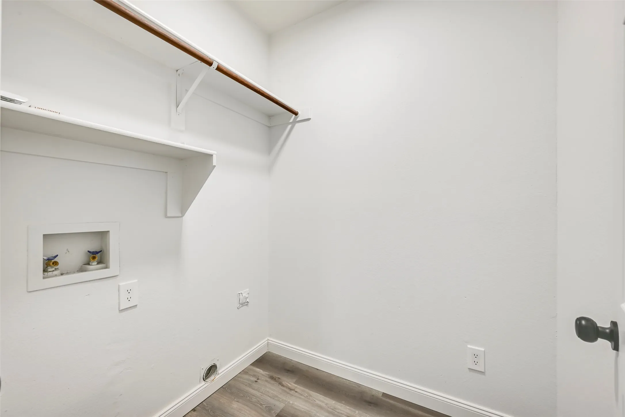 Dedicated utility area featuring white walls, a built-in shelf, a hanging rod, wood-finish flooring, and white baseboards