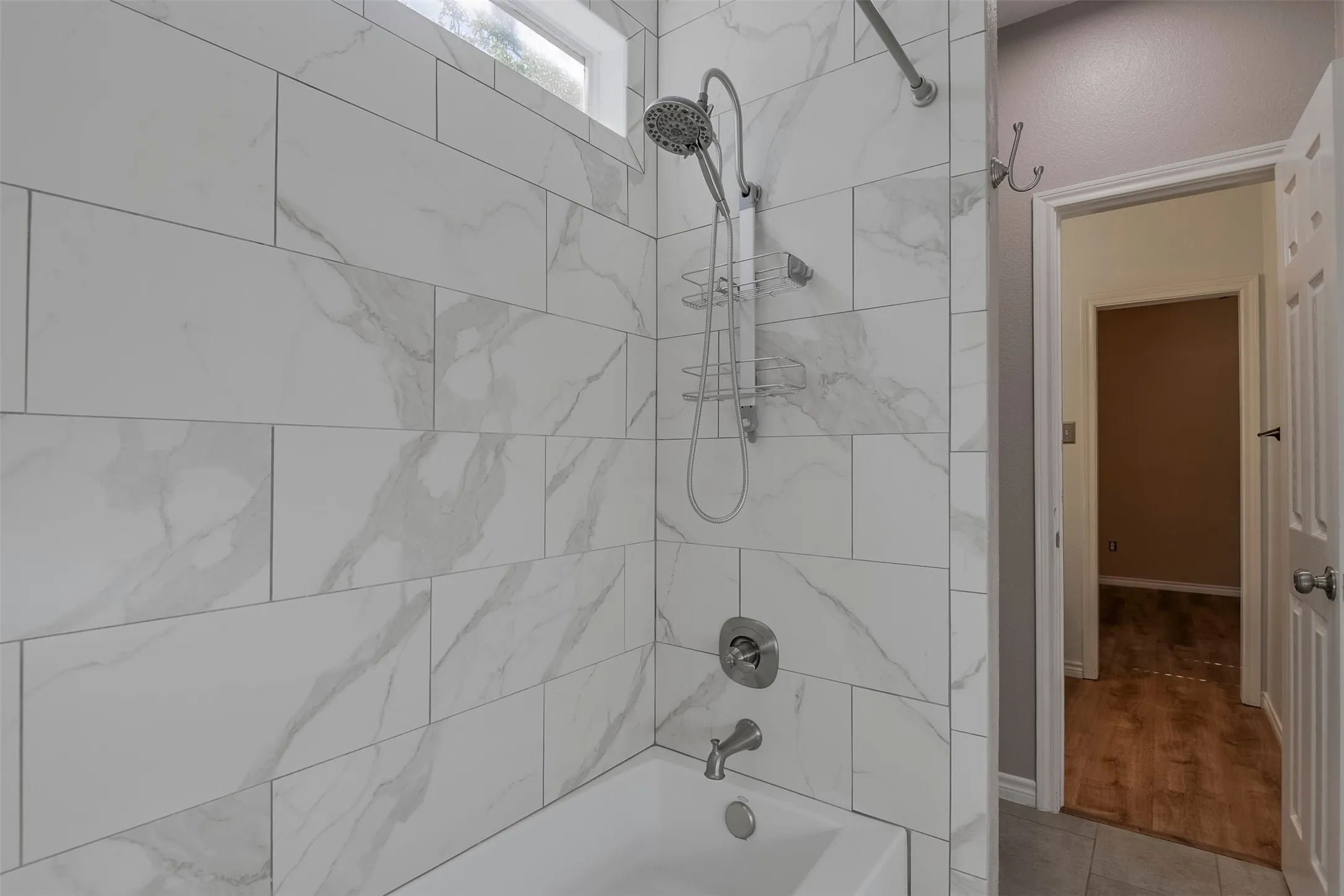 Bathtub shower with white rectangular tile surround, rainfall showerhead, handheld shower fixture, and brushed nickel hardware