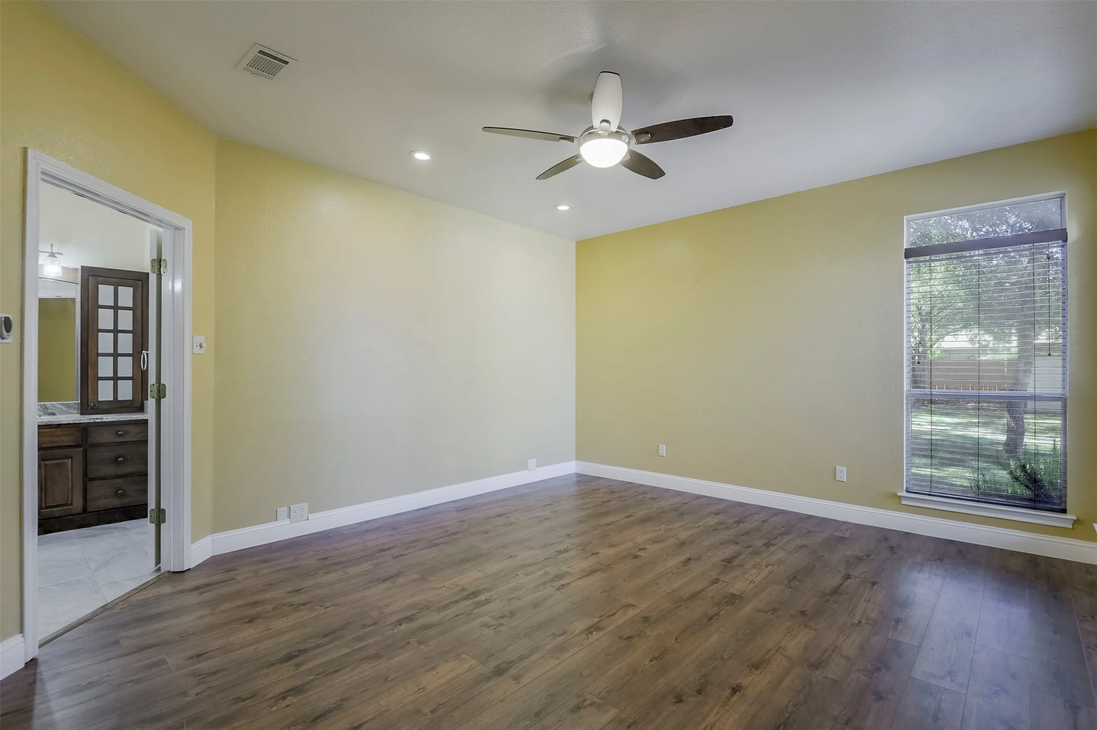 Spacious room featuring wood-finish flooring, a ceiling fan with integrated lighting, recessed lighting, and a large window with blinds