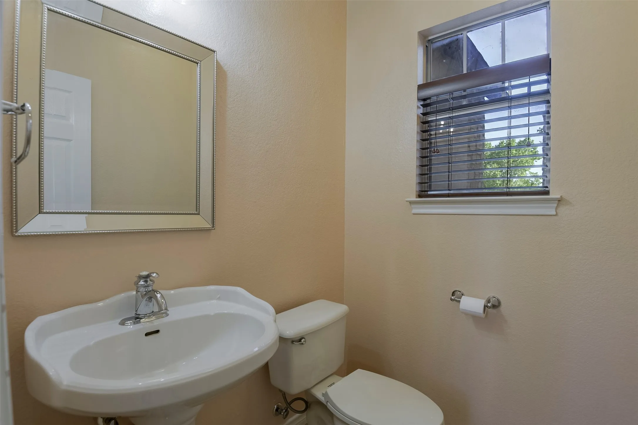 Pedestal sink with chrome faucet, complemented by a decorative framed mirror