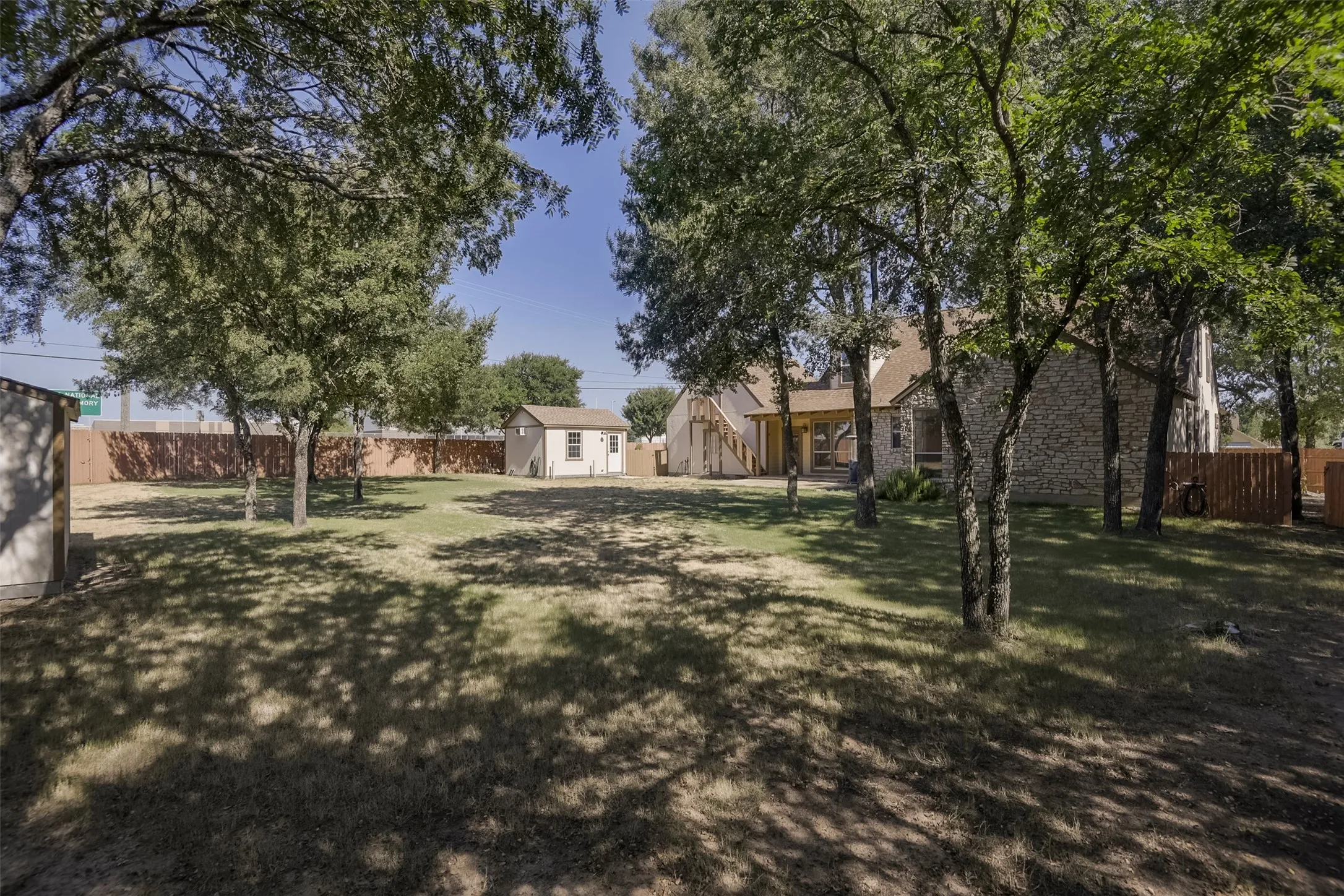 Expansive backyard featuring mature trees, a wooden privacy fence, a detached storage shed, and a brick-sided residence with an outdoor covered patio