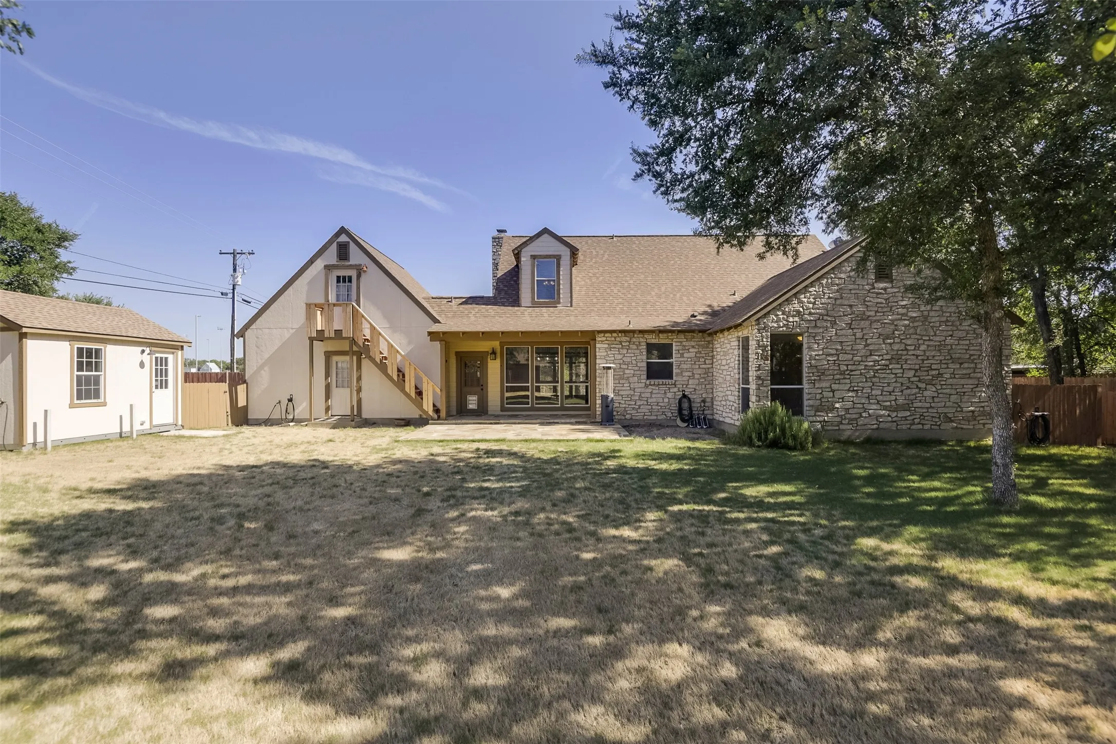 Rear exterior featuring stone and stucco finishes, a detached storage building, an exterior staircase, and a covered patio area with multiple glass doors