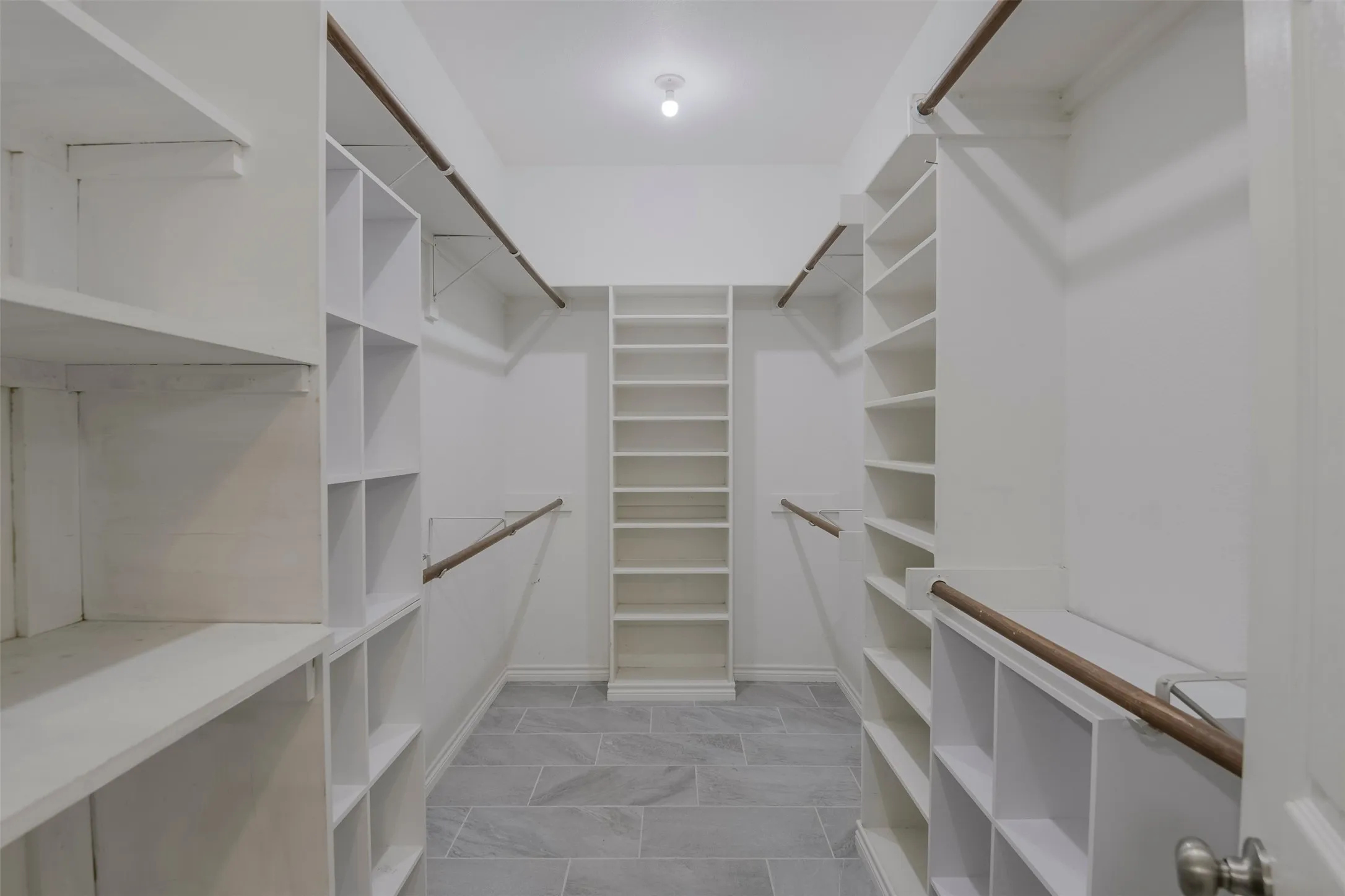 Spacious walk-in closet featuring white built-in shelving, hanging rods, and grey tile flooring