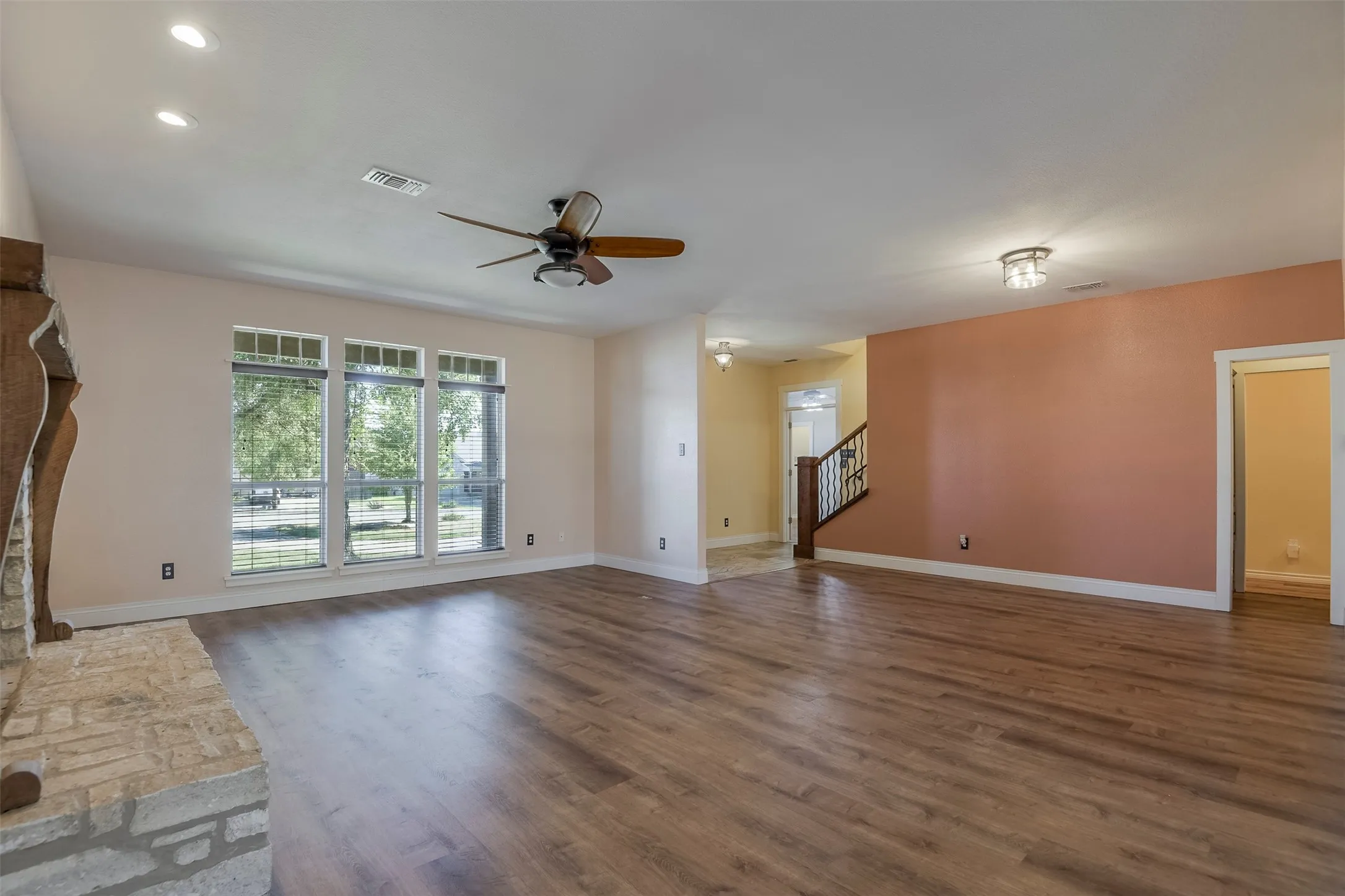 Spacious living area featuring wood-finish flooring, a stone fireplace with decorative wood mantel, and multiple windows