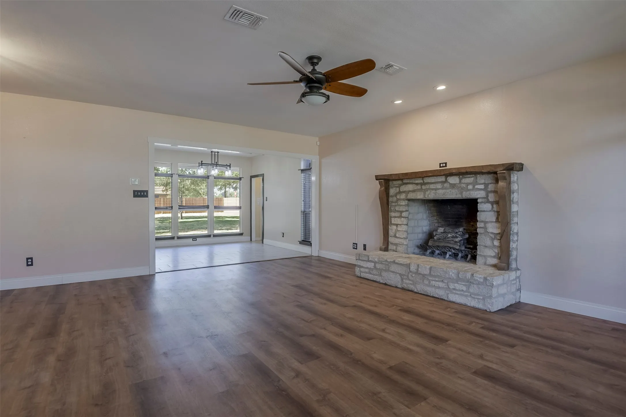 Spacious living area featuring wood-finish flooring and a stone-clad fireplace with a substantial timber mantel