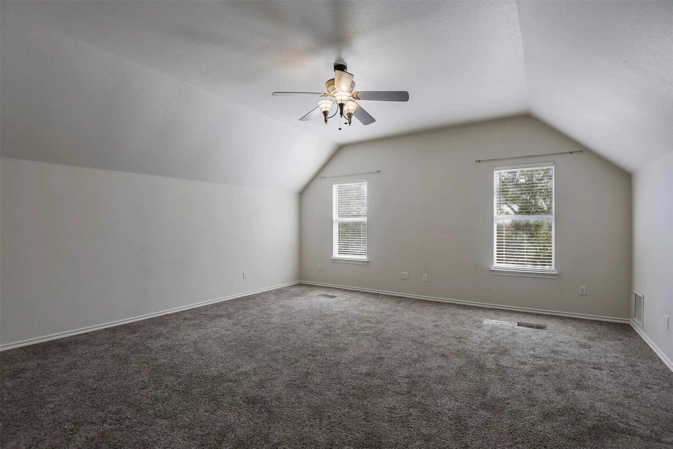 Spacious room featuring vaulted ceilings, neutral wall tones, and plush carpeting