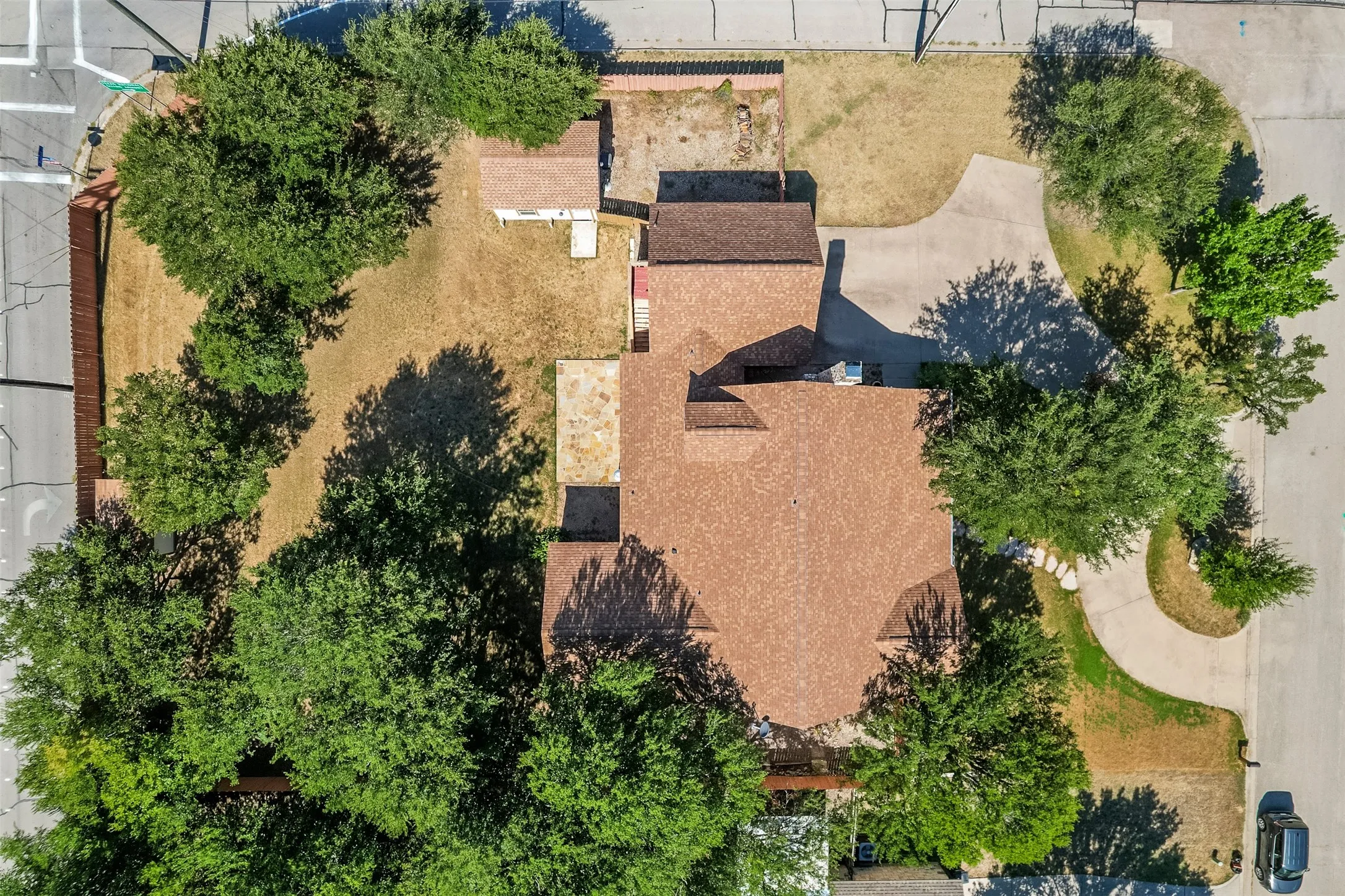 Residential property featuring a brown shingle roof, mature trees, concrete driveway, and a detached outbuilding