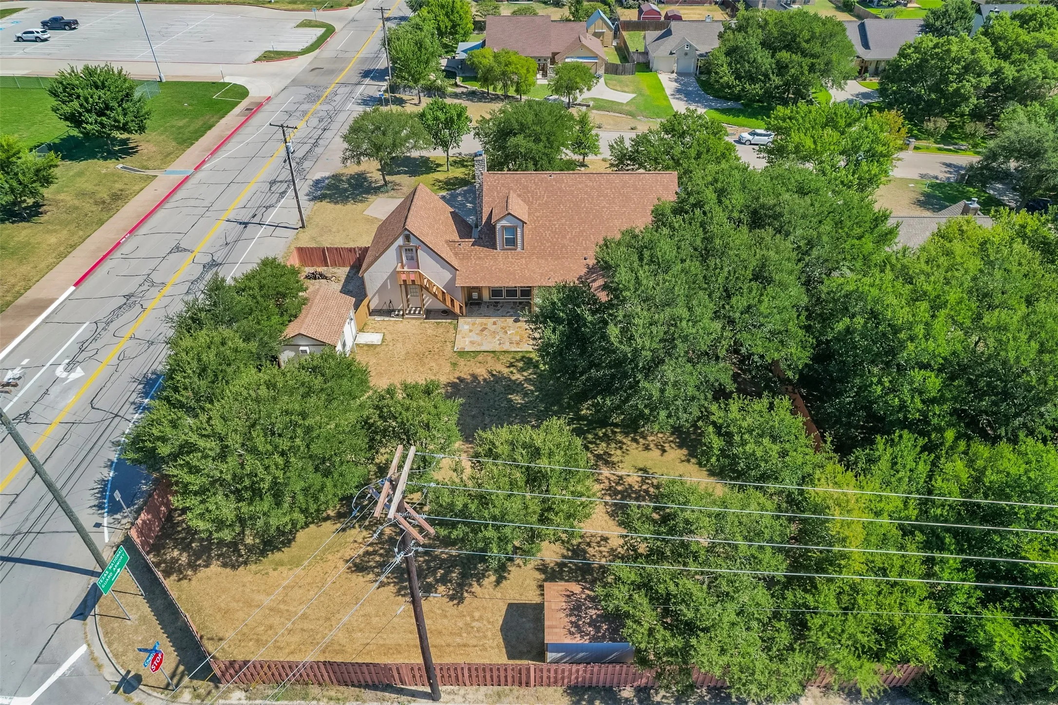 Expansive property featuring a brown shingle roof, mature perimeter trees, a detached storage shed, and a brown privacy fence