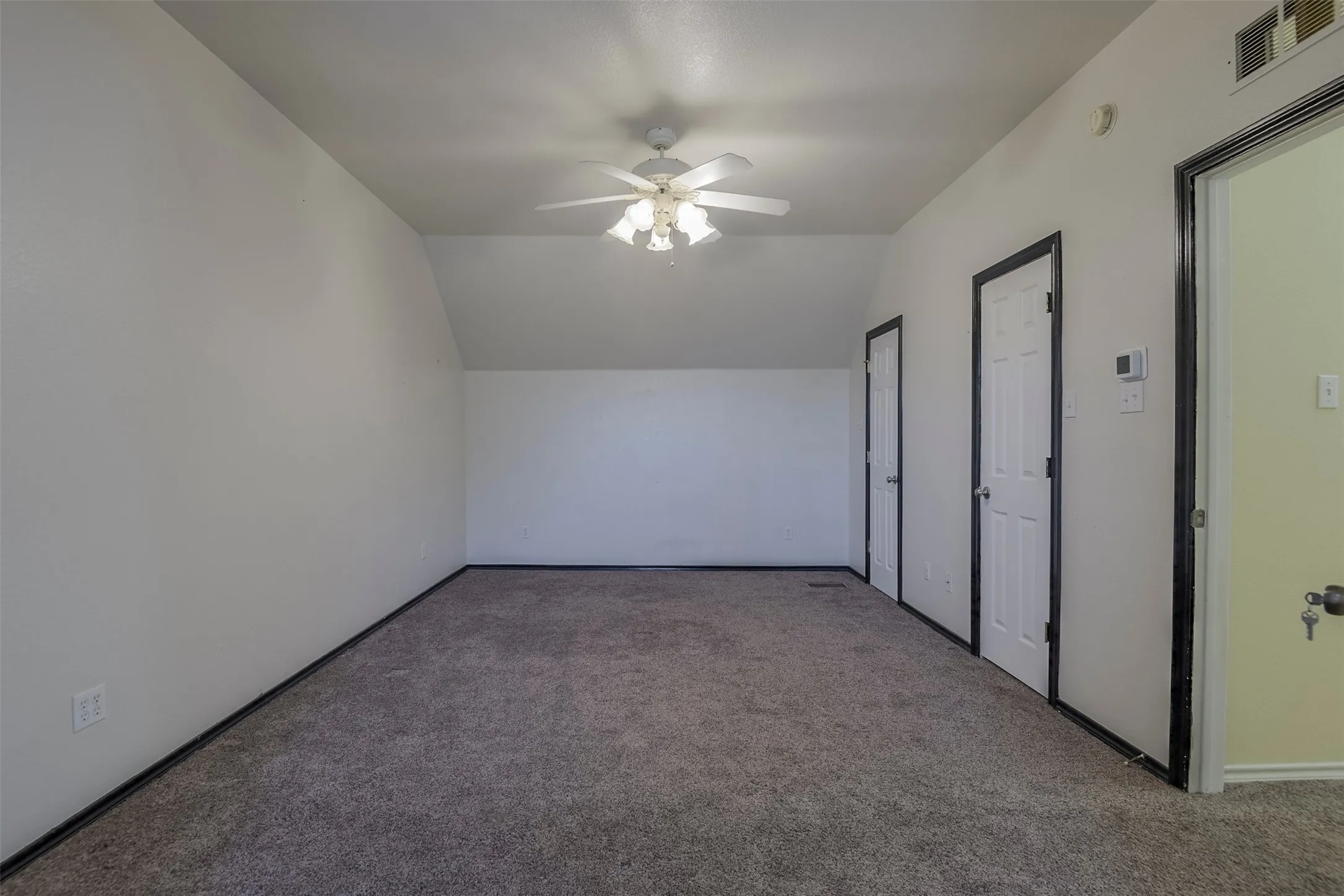 Spacious room featuring gray carpeting, white walls, a ceiling fan with integrated lighting, and multiple white paneled doors with contrasting dark trim