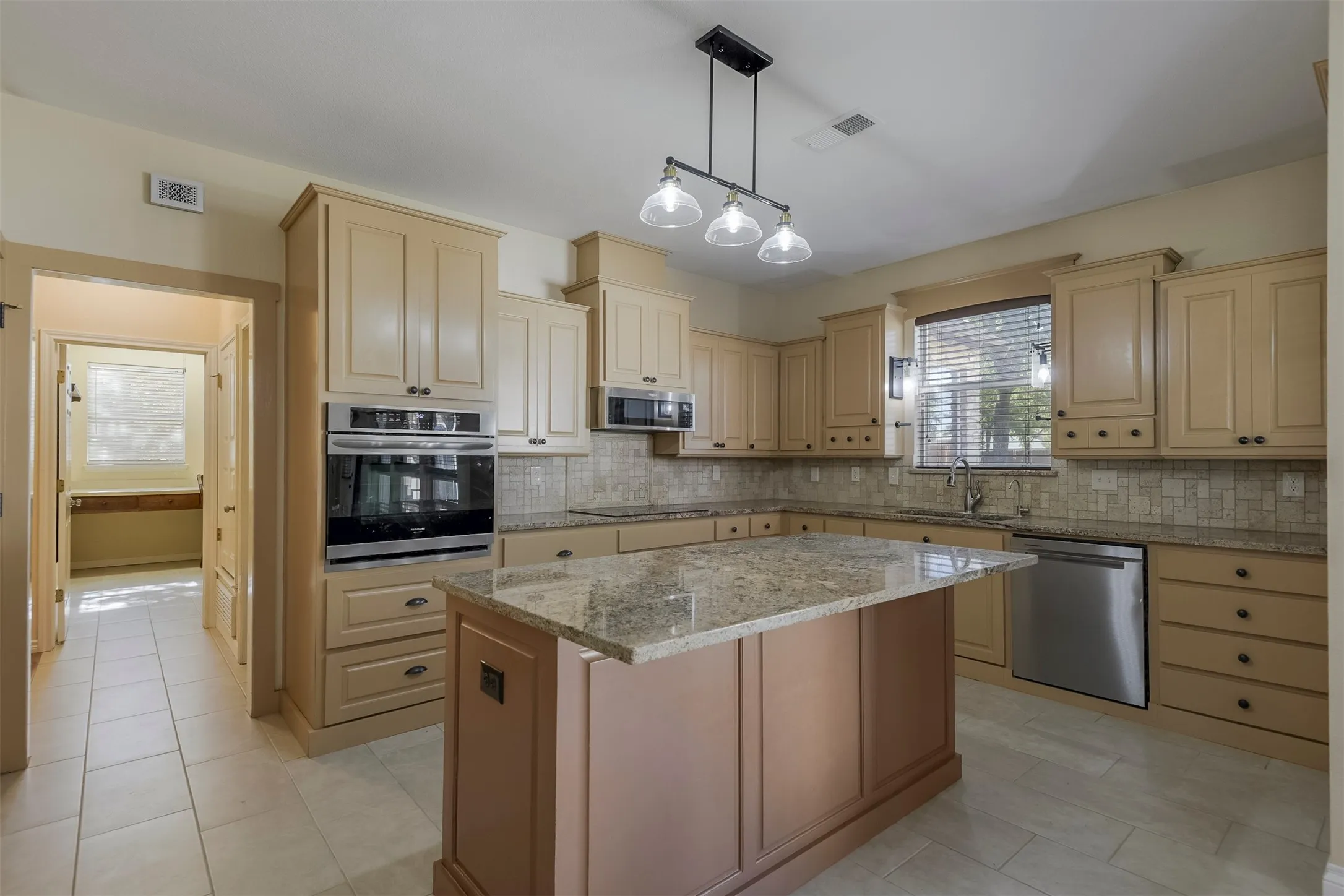 Spacious kitchen featuring a central island with a stone countertop, extensive cabinetry, stainless steel appliances, and tile flooring