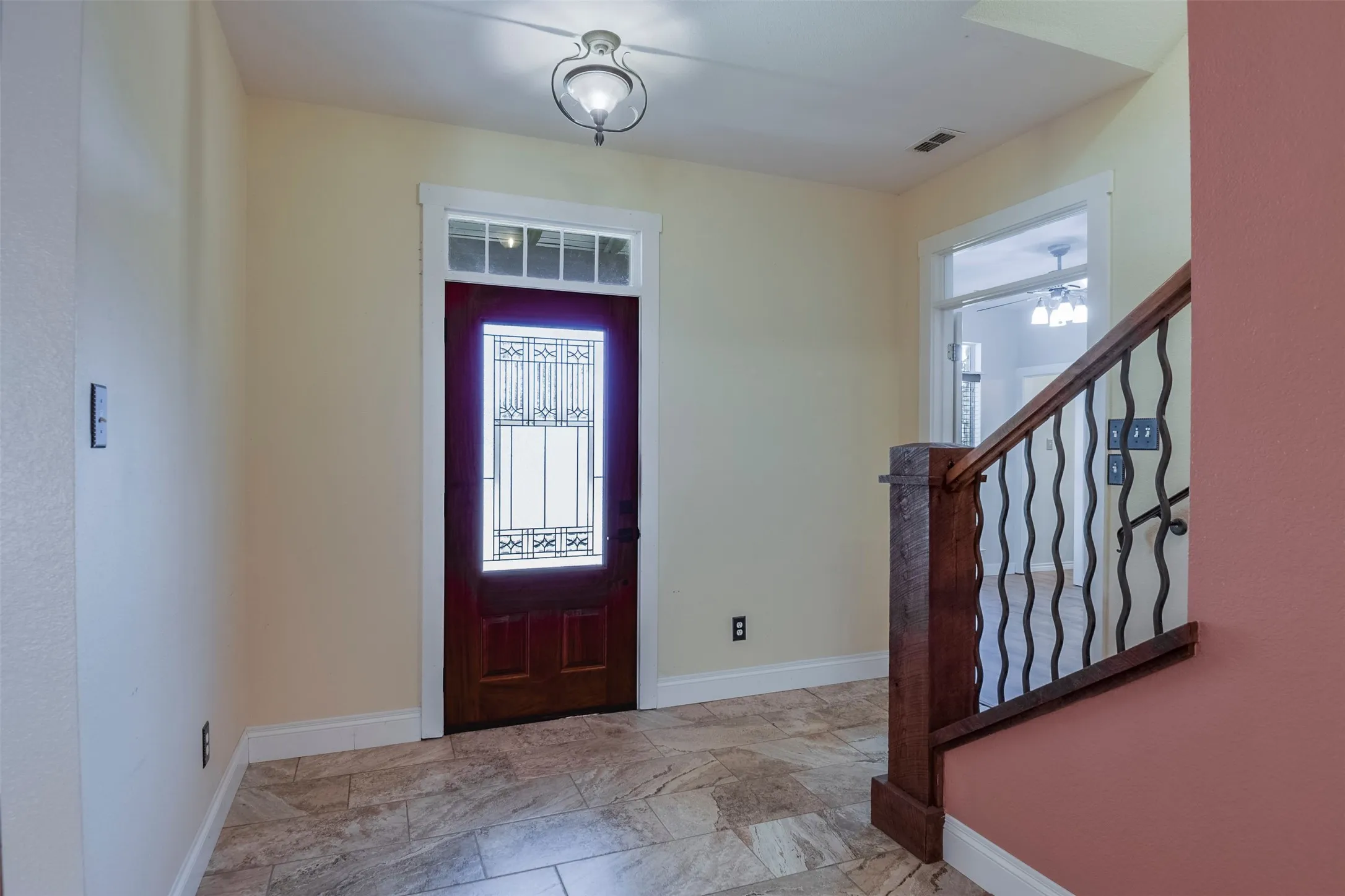Foyer featuring tile flooring, a wood entry door with decorative glass inserts and transom, and a staircase with a wood handrail and wrought iron balusters