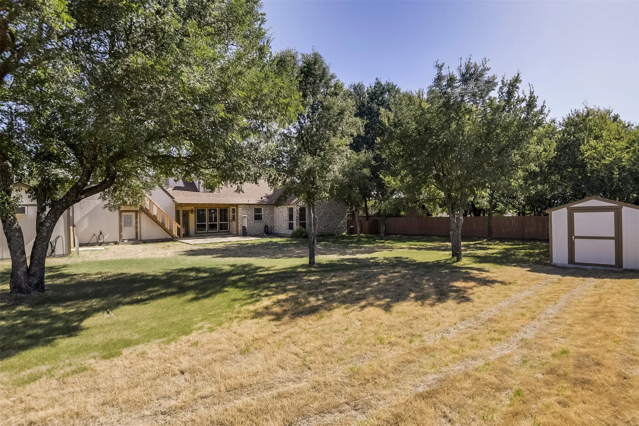 Expansive backyard featuring mature trees, a storage shed, and a privacy fence