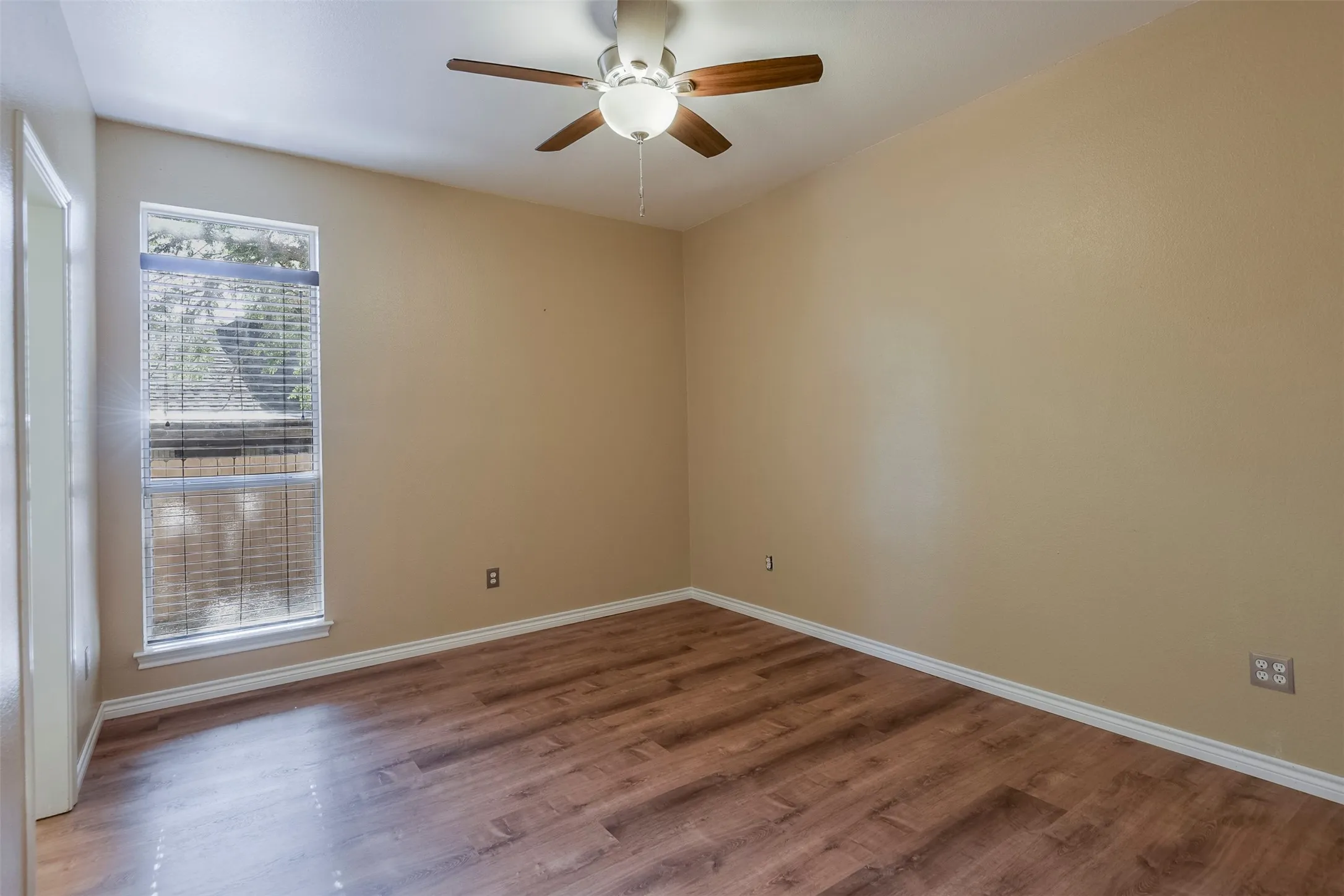 Room featuring wood-finish flooring, a ceiling fan with integrated lighting, and a window with horizontal blinds