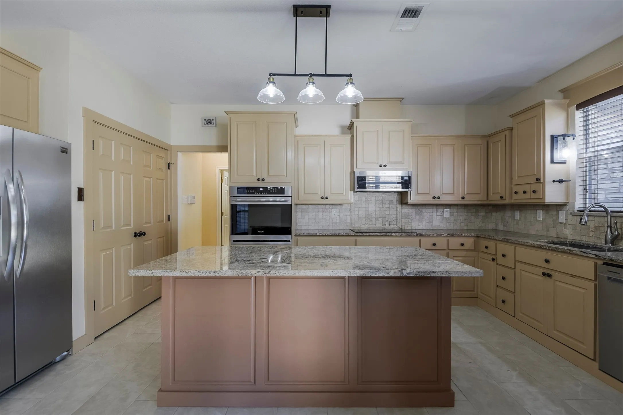 Kitchen featuring a center island with a granite countertop, light-toned cabinetry, stainless steel appliances, and a tiled backsplash