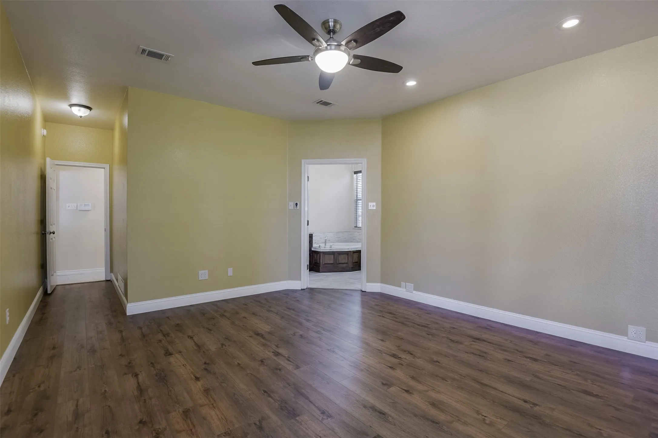 Spacious room featuring wood-finish flooring, recessed lighting, and a ceiling fan with integrated light