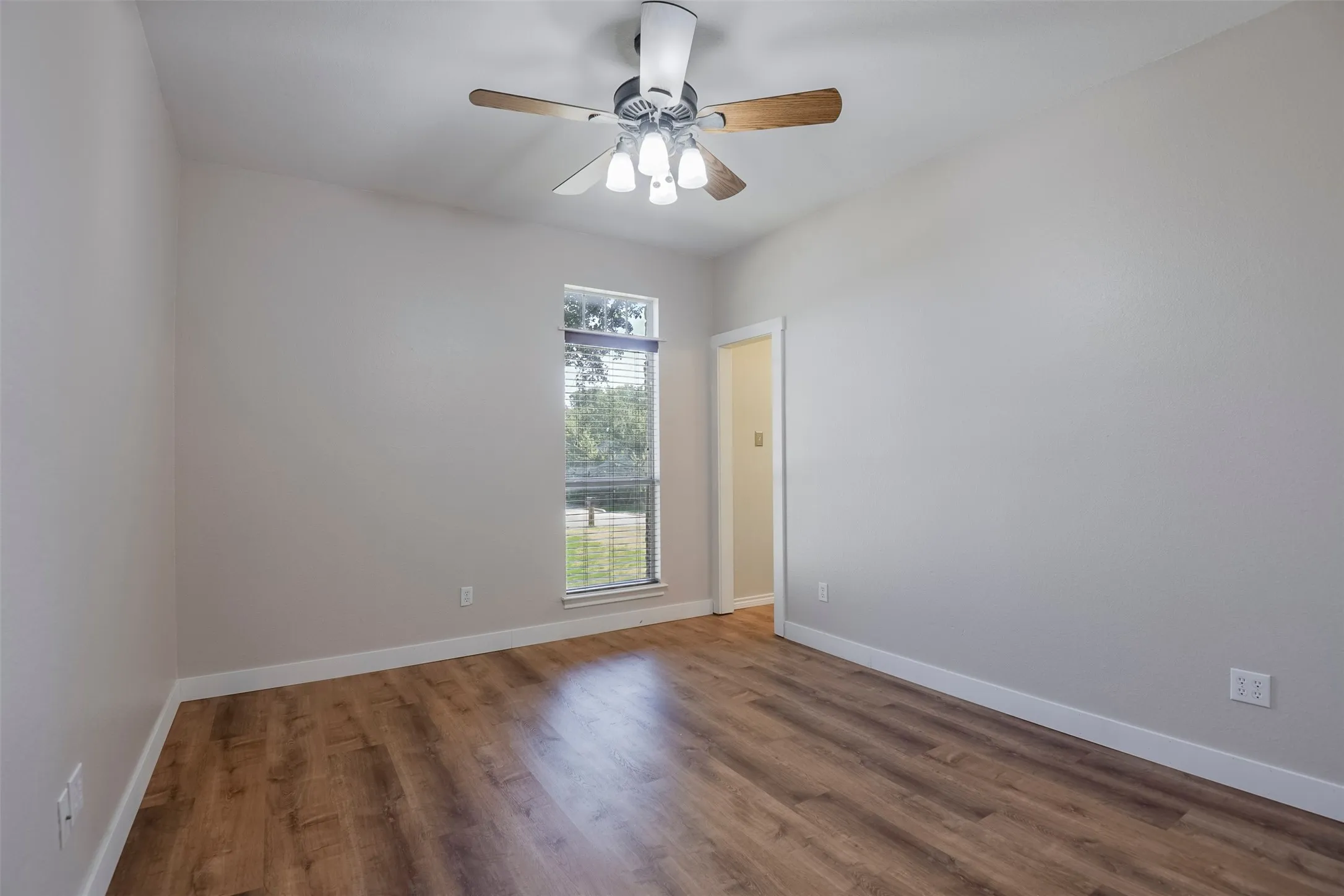 Room featuring wood-finish flooring, a ceiling fan with integrated lighting, a window with horizontal blinds, and a neutral wall color