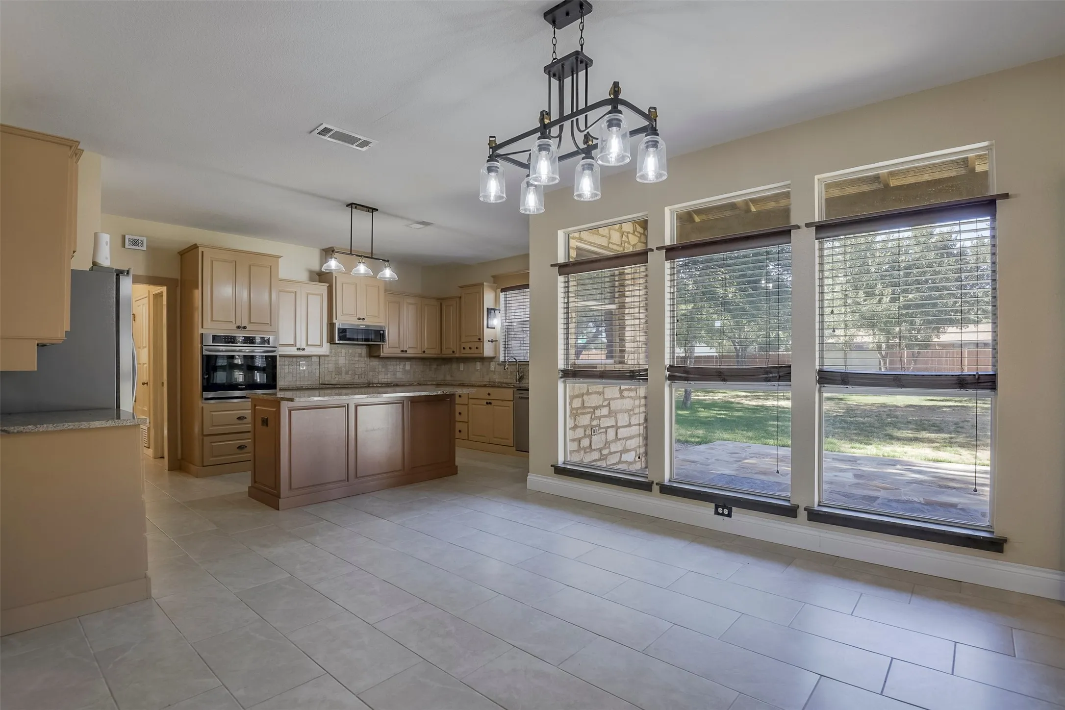 Spacious kitchen and dining area featuring ceramic tile flooring, a large kitchen island with built-in cabinetry, stainless steel double ovens, and extensive cabinetry throughout