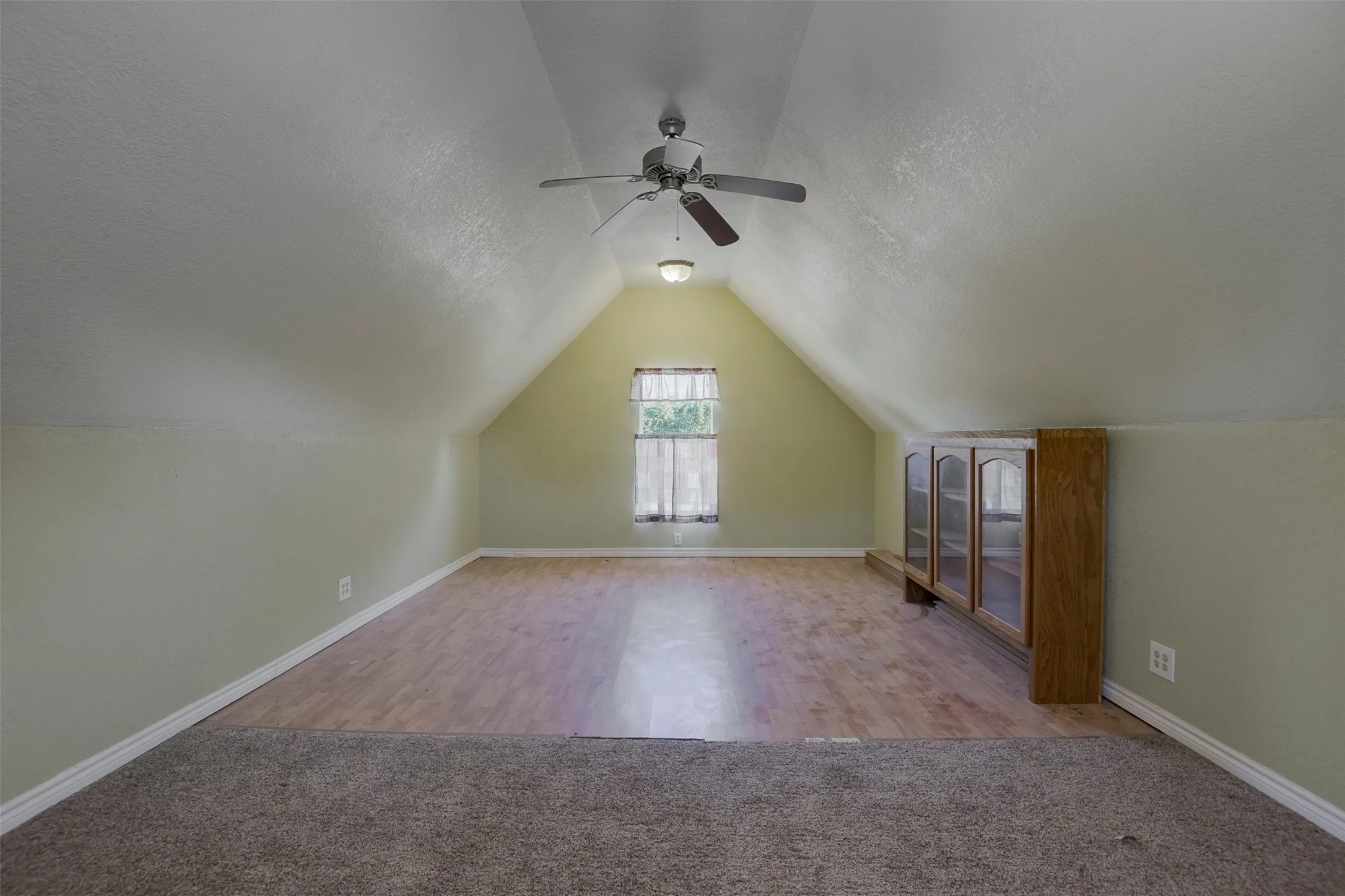 Spacious room with a vaulted ceiling, wood-finish flooring, and light green walls