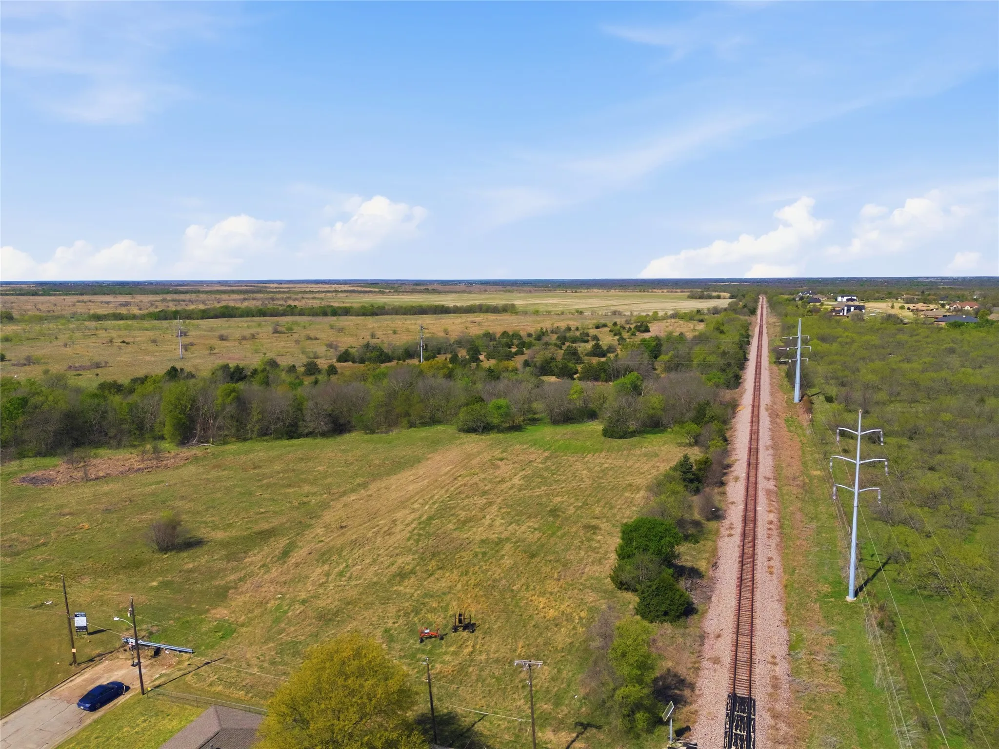 Expansive undeveloped land featuring a railroad track, mature trees, and a clear sky