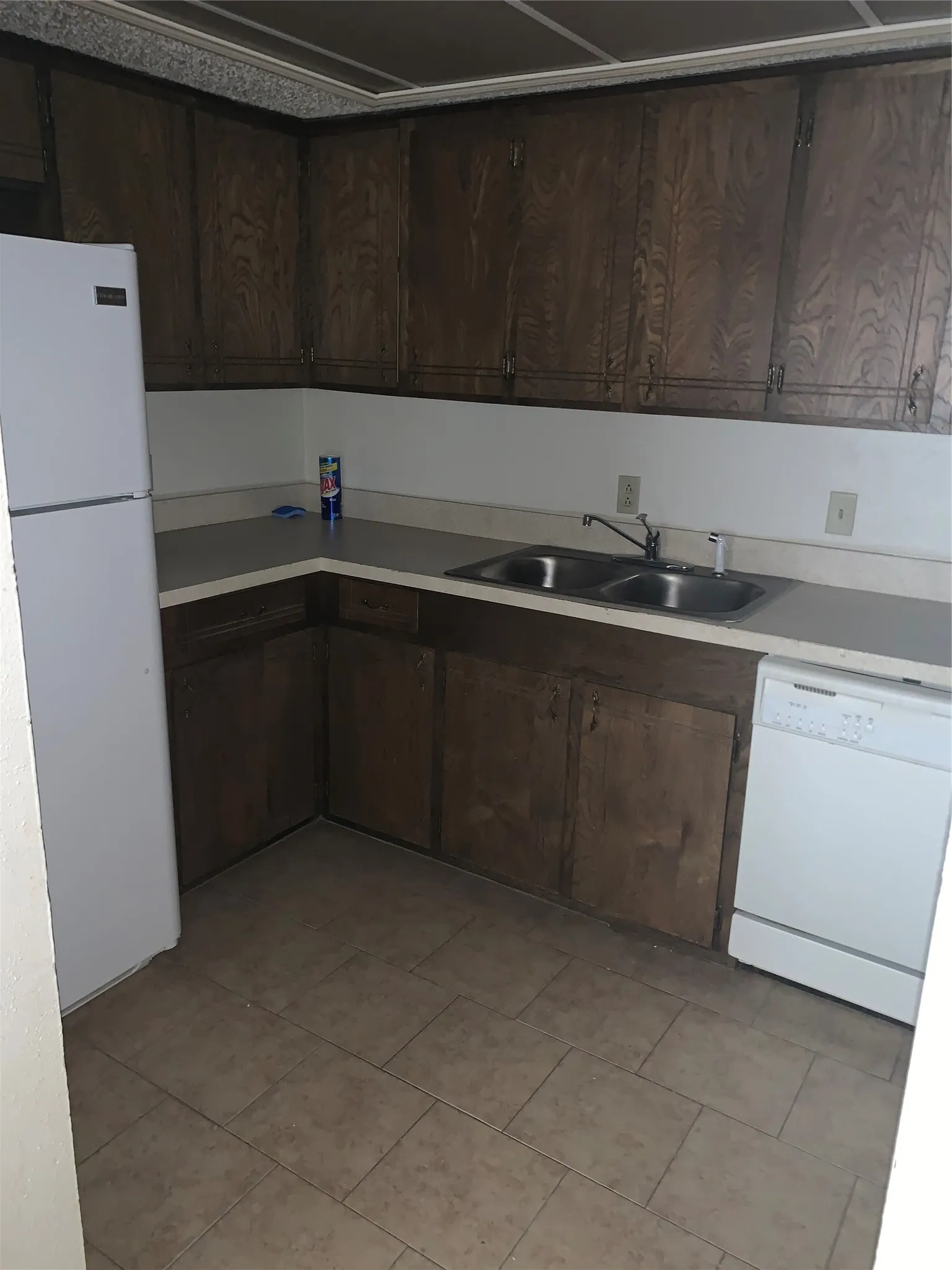 Kitchen featuring a double basin stainless steel sink, wood-finish cabinetry, light-toned countertops, and tile flooring